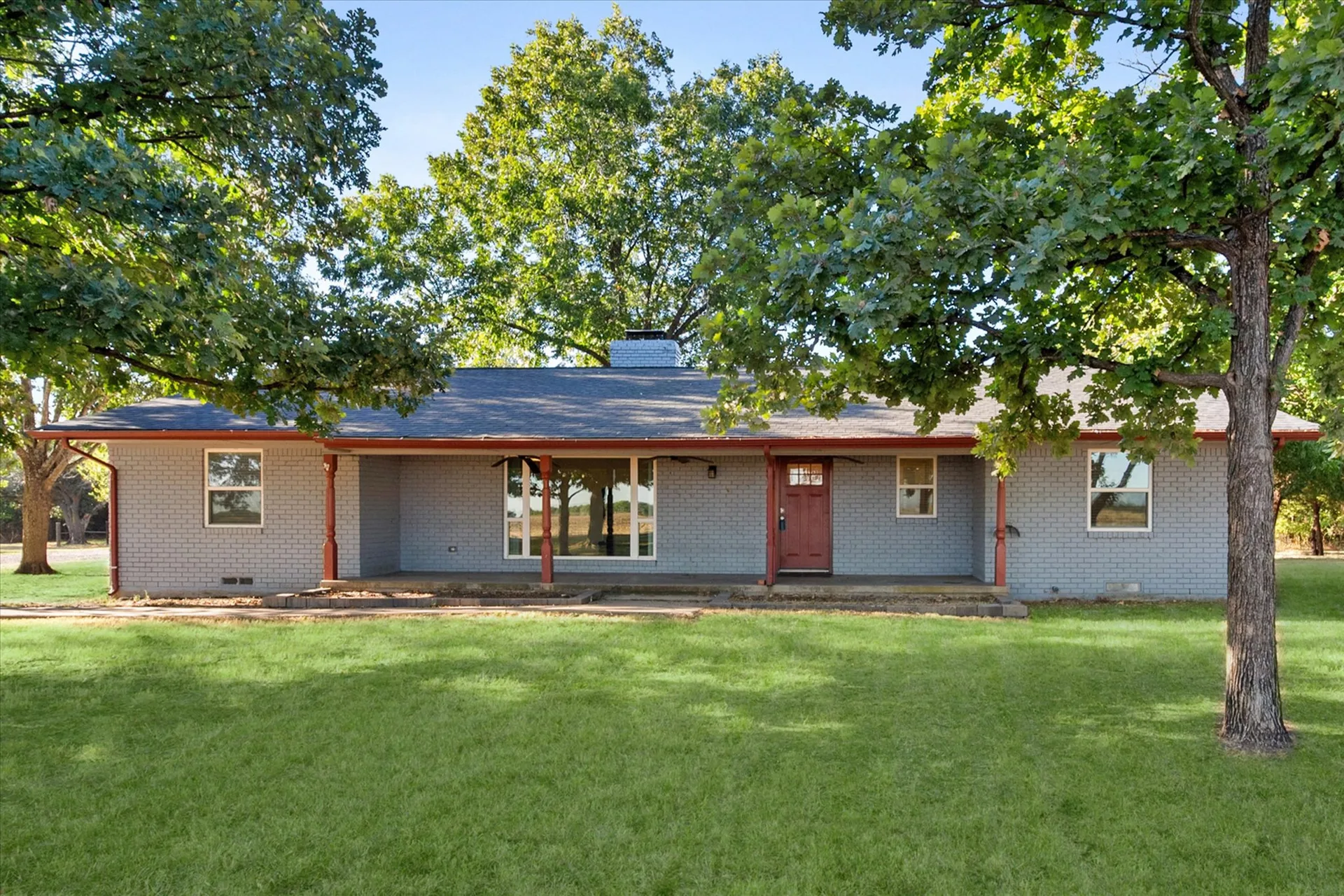 Front facade of the gray brick ranch home shaded by mature oaks