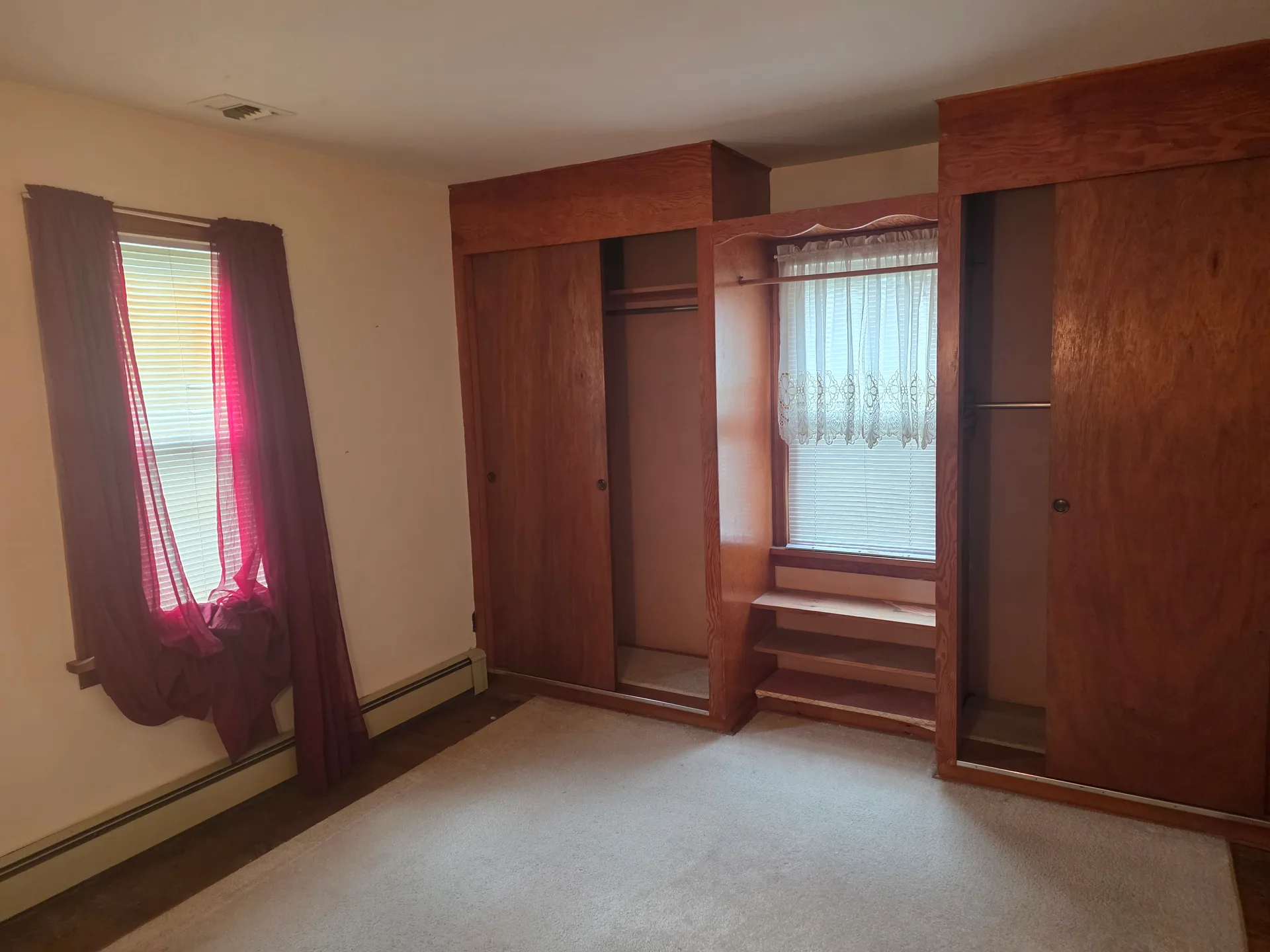 Bedroom with beige walls, carpeted floor, and built-in wooden closet units