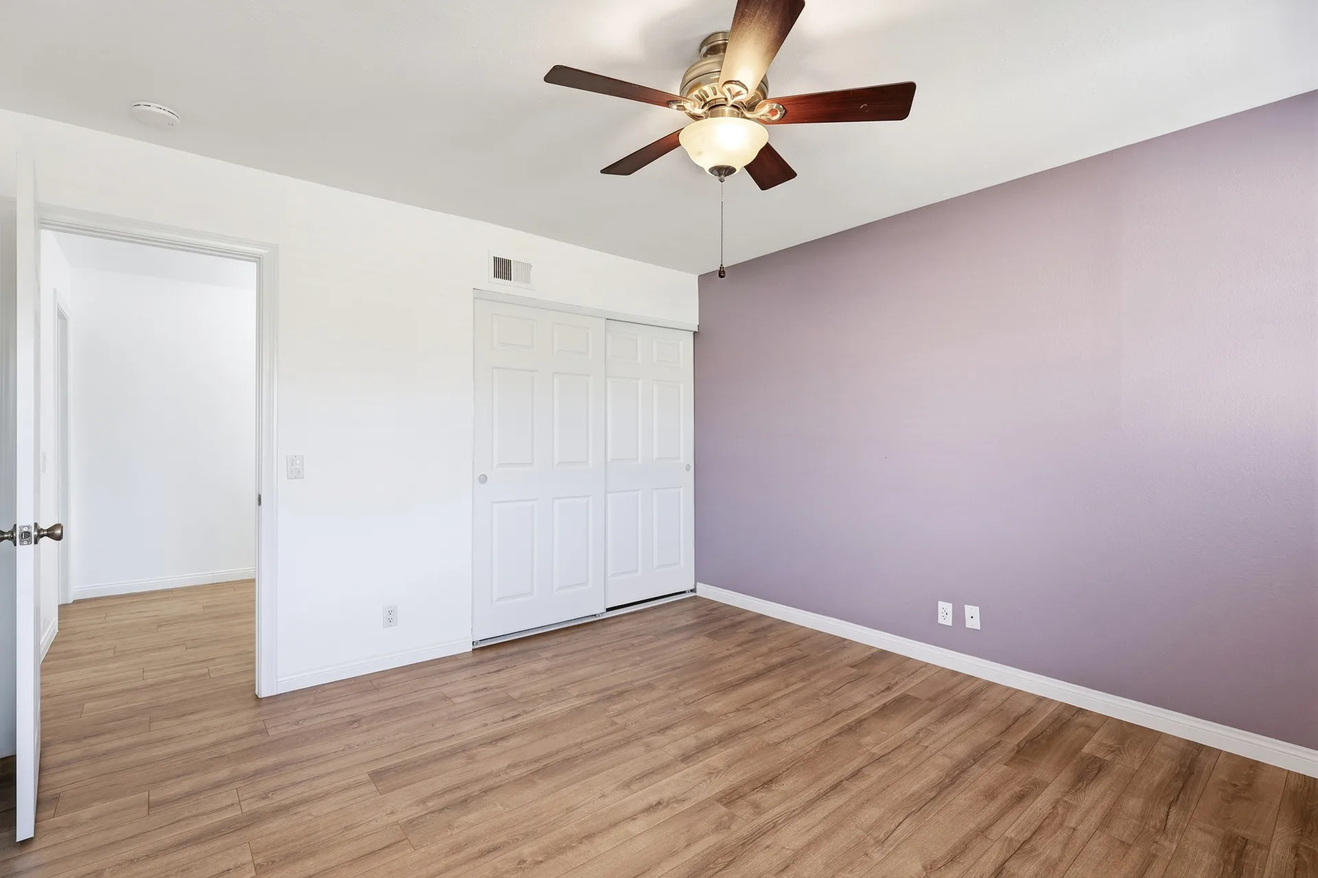 Primary bedroom at 8 Silverwood with a lavender accent wall, wood-look flooring, and bright natural light