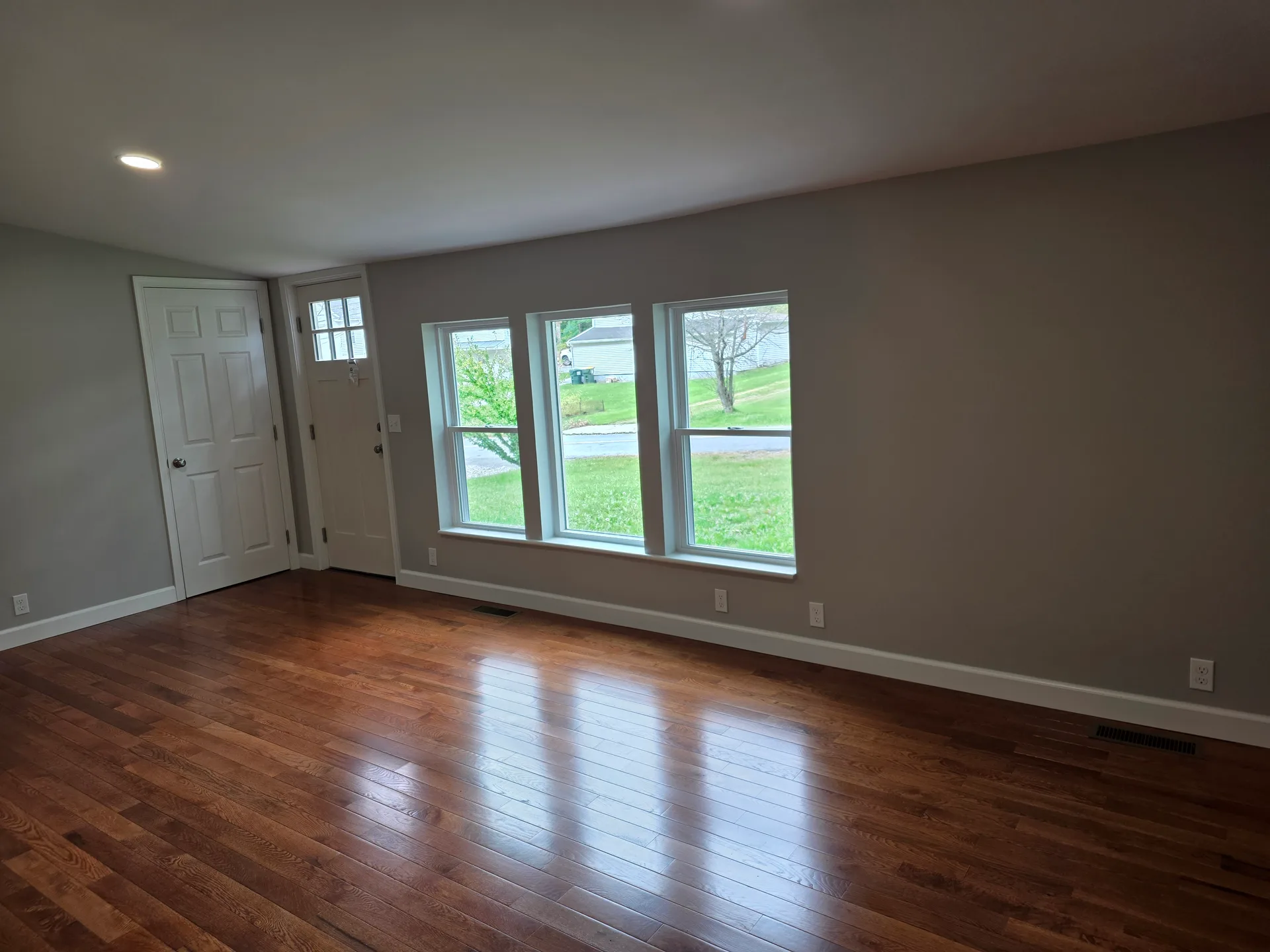 Bright living room with hardwood floors, light grey walls, and large windows