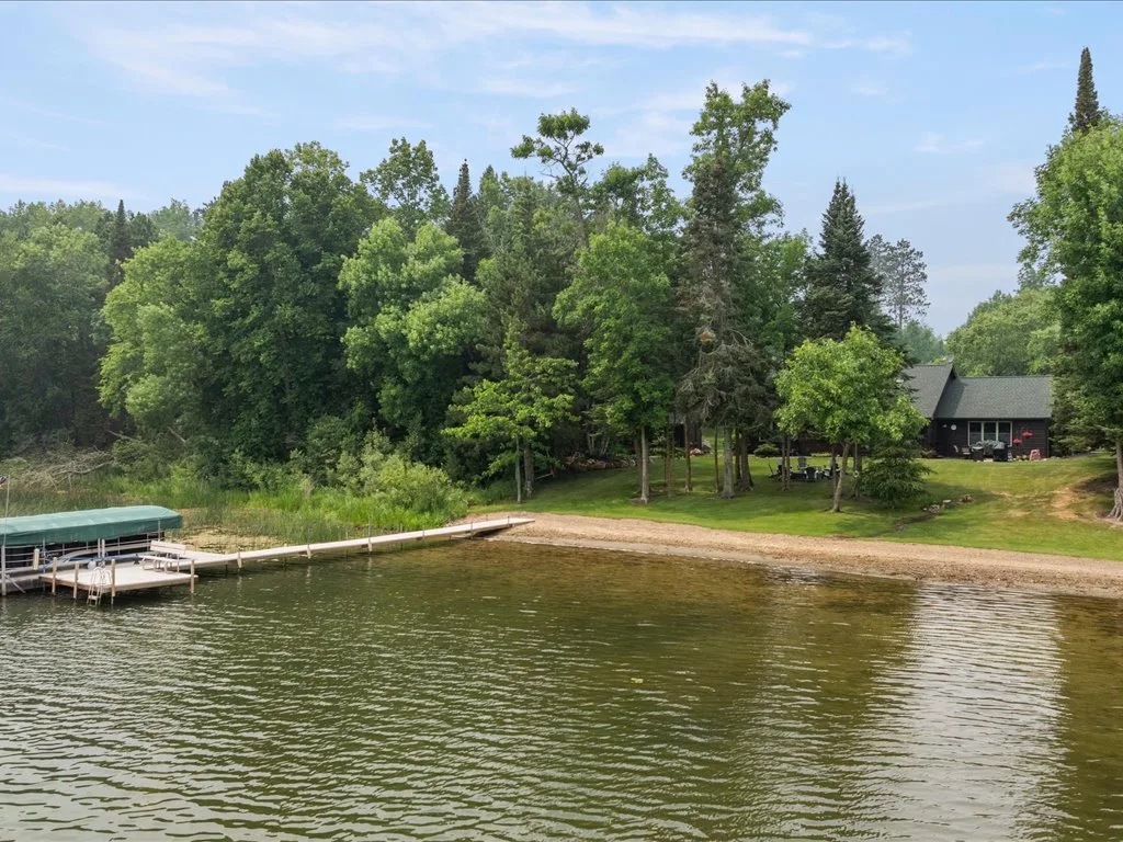 Angled view from the water of the dock, boat lift, and dark-siding lake home