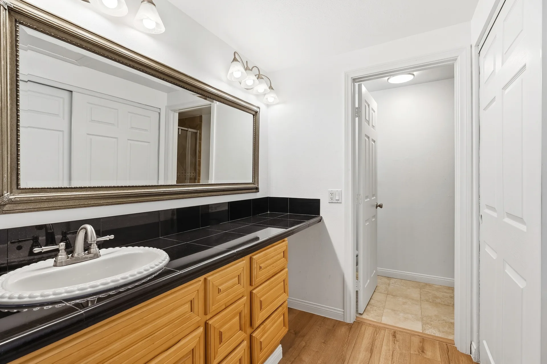 Bathroom vanity at 8 Silverwood with wood cabinetry, a black tile counter, and a framed mirror