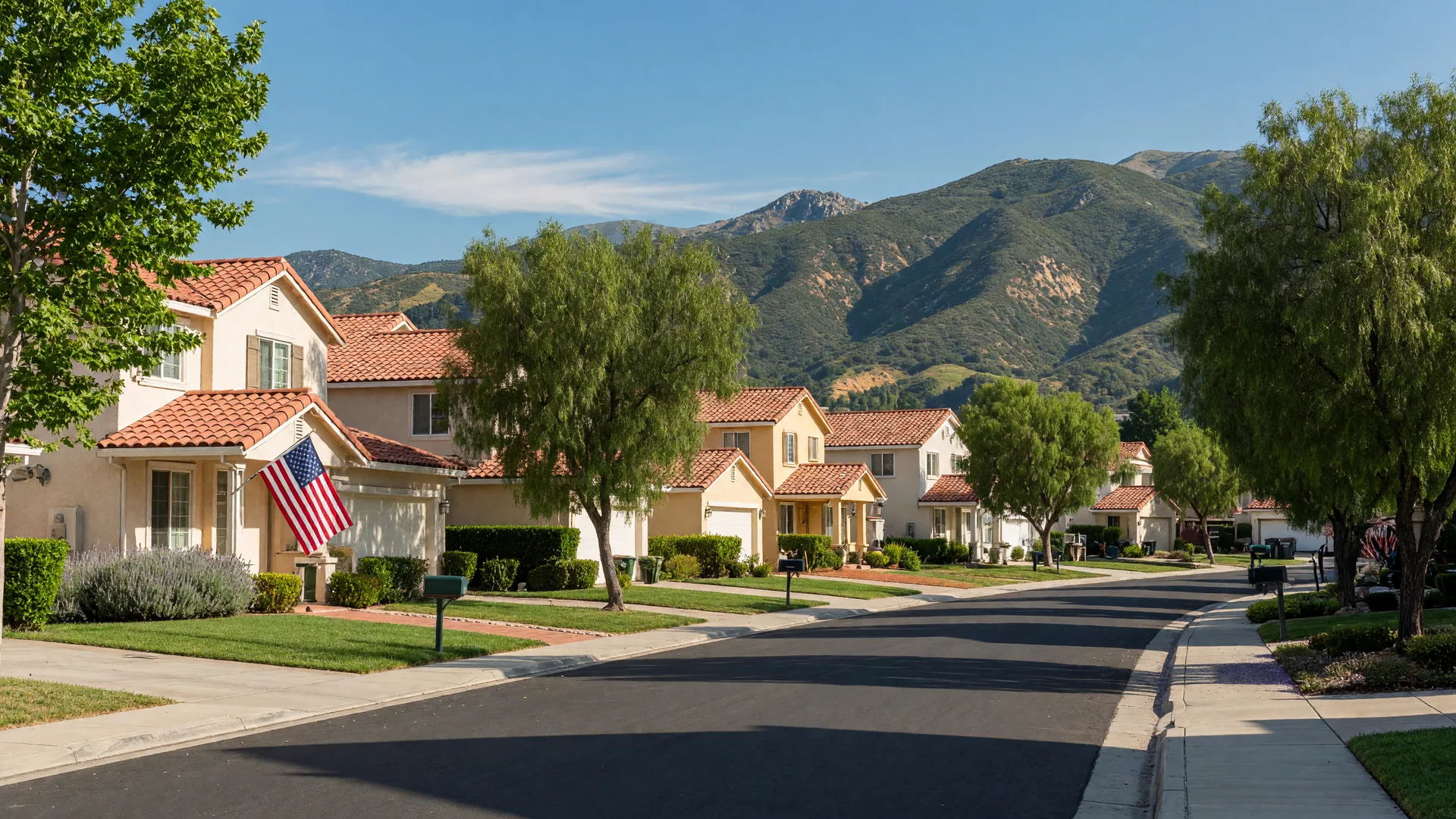 A sunny Santa Clarita Valley neighborhood street with homes, an American flag on a porch, and mountains in the distance
