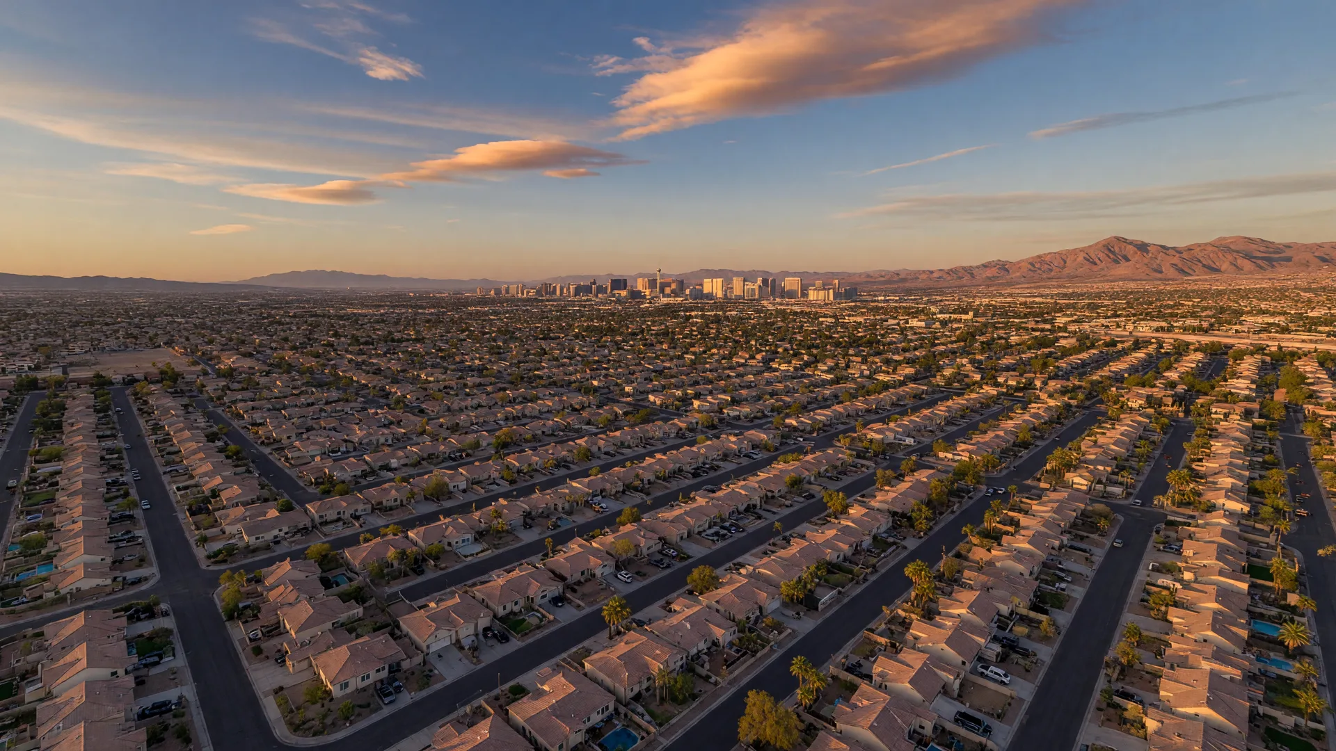 Aerial view of Las Vegas suburban neighborhoods at golden hour with Strip skyline and mountains in the distance