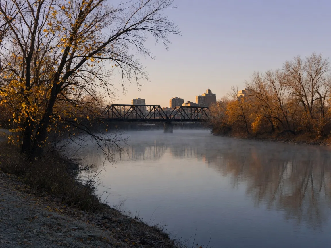 The Illinois River waterfront in Peoria in early November, with bare trees, thin frost haze, and a truss bridge in the distance under late-afternoon light