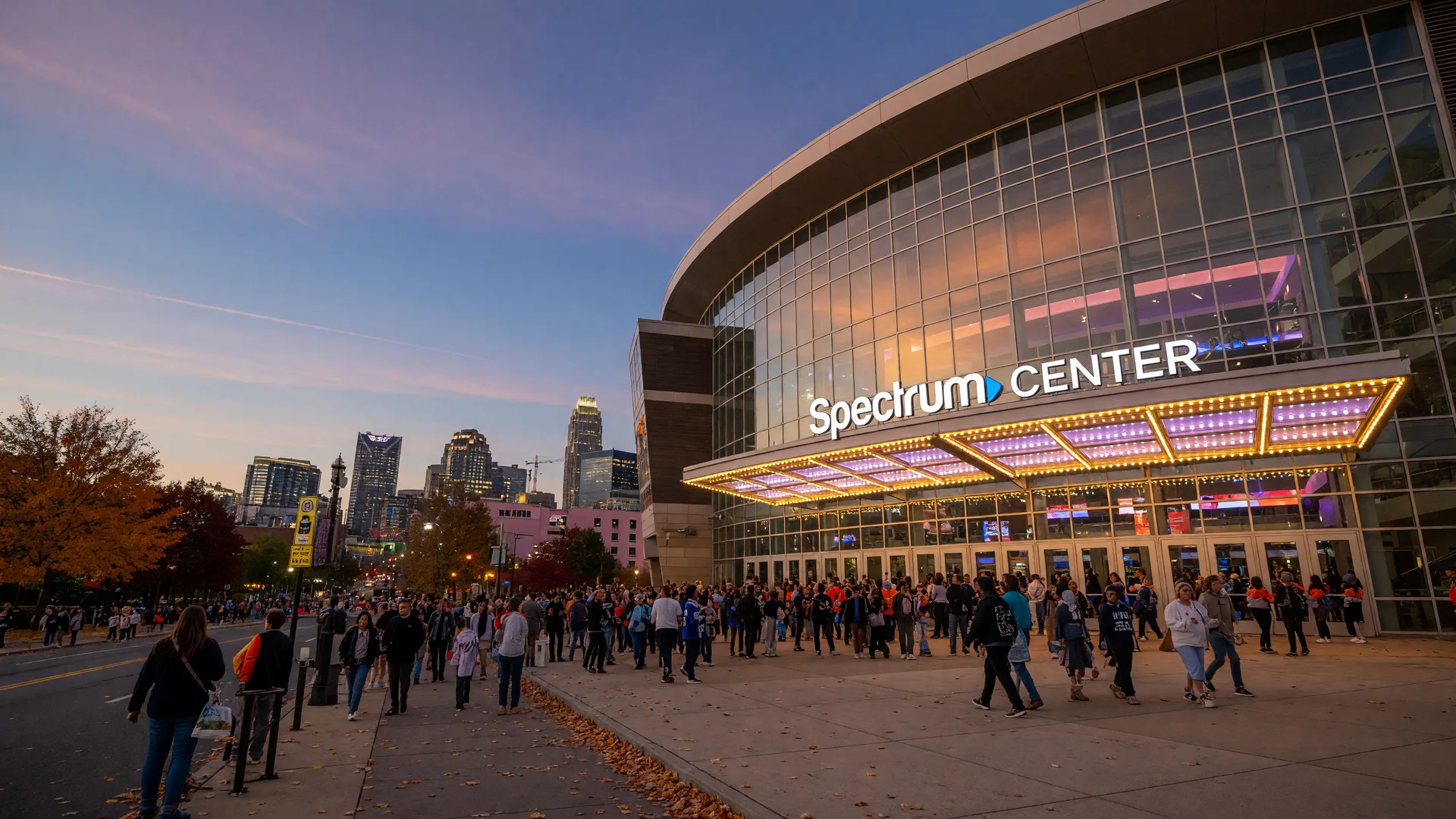 Spectrum Center in Uptown Charlotte on an October evening with fans approaching the entrance beneath glowing lights and a twilight sky