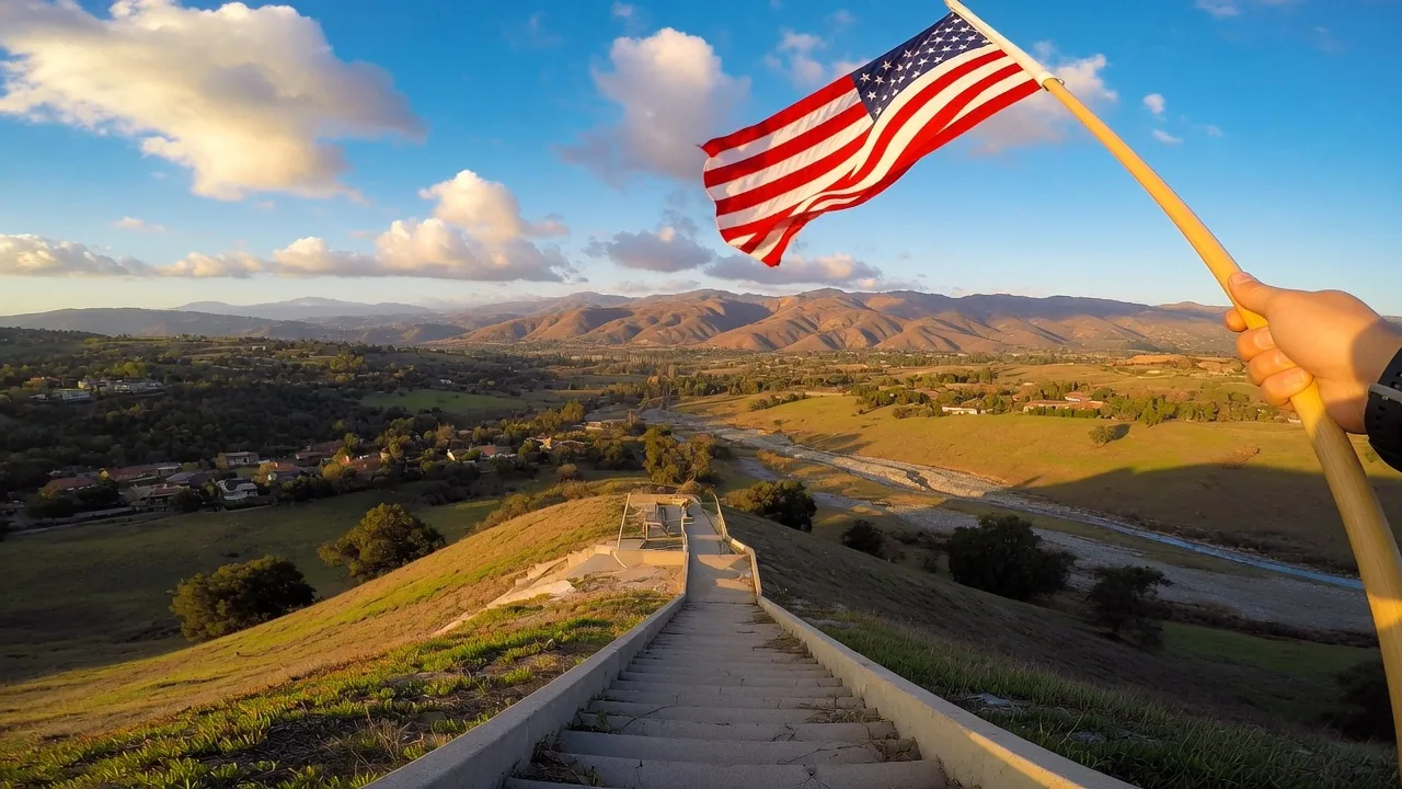 Selfie view from the top of the SCV Stairs with an American flag waving against a blue sky overlooking the Santa Clarita Valley.