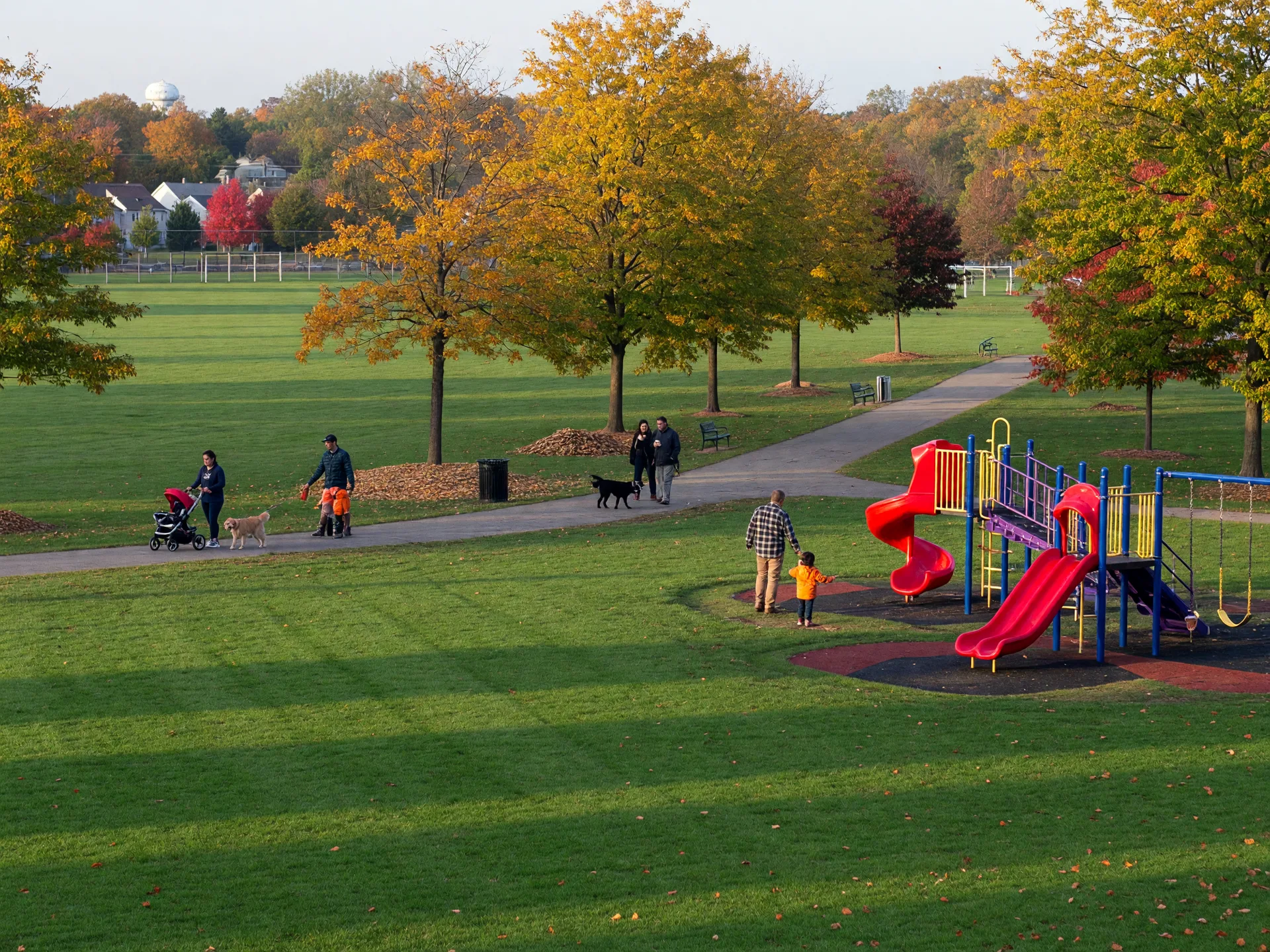 A well-kept township park in South Jersey on a sunny October morning with a green playing field, playground, and tree-lined walking paths in fall color