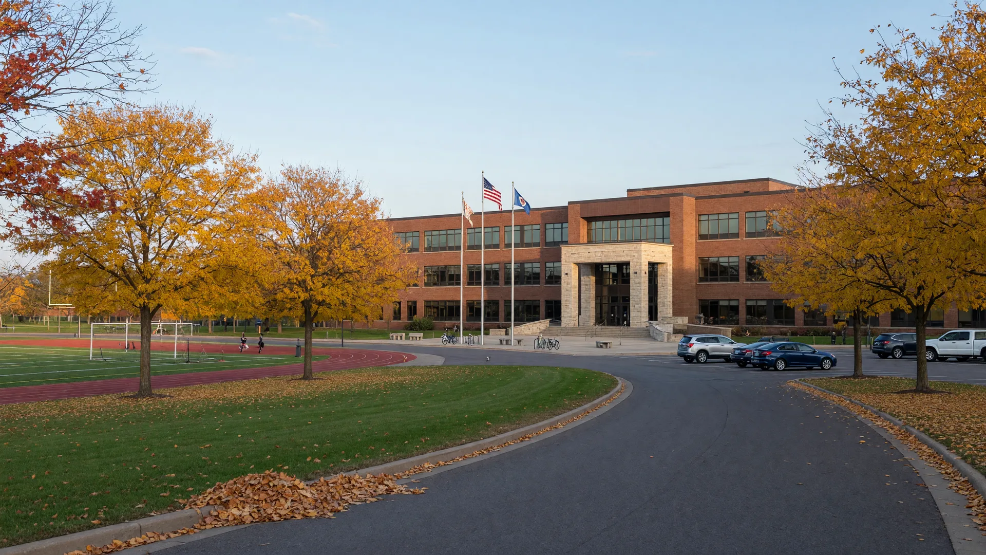 Modern Minnesota high school campus with brick and glass buildings, a stone entrance, and golden maples in early October