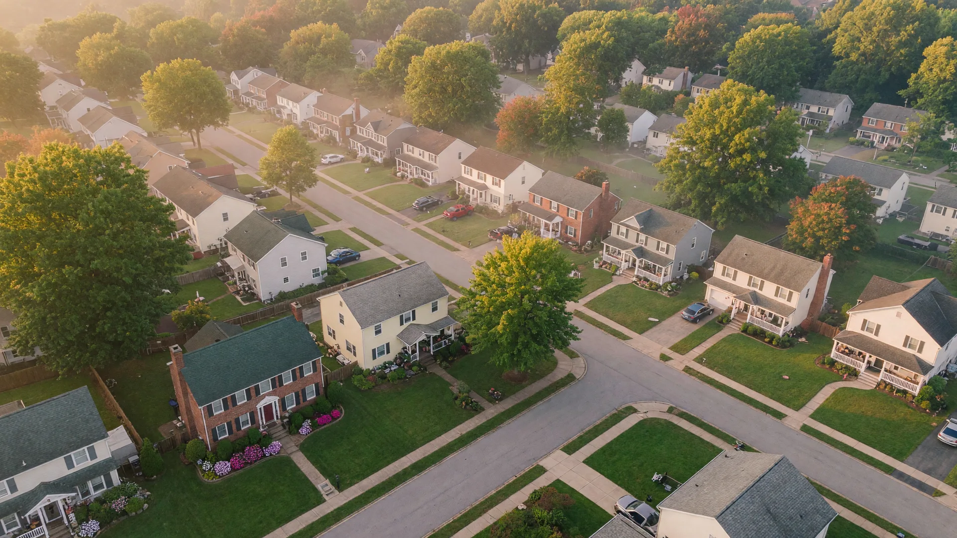 A leafy residential neighborhood at dawn with neatly kept homes along tree-lined streets