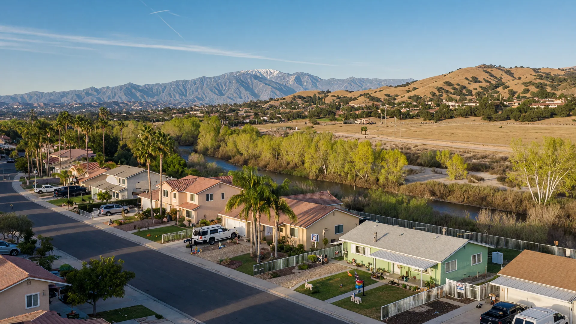 Jurupa Valley suburban street with newer stucco homes and older ranch-style properties, the Santa Ana River corridor and hills in the distance