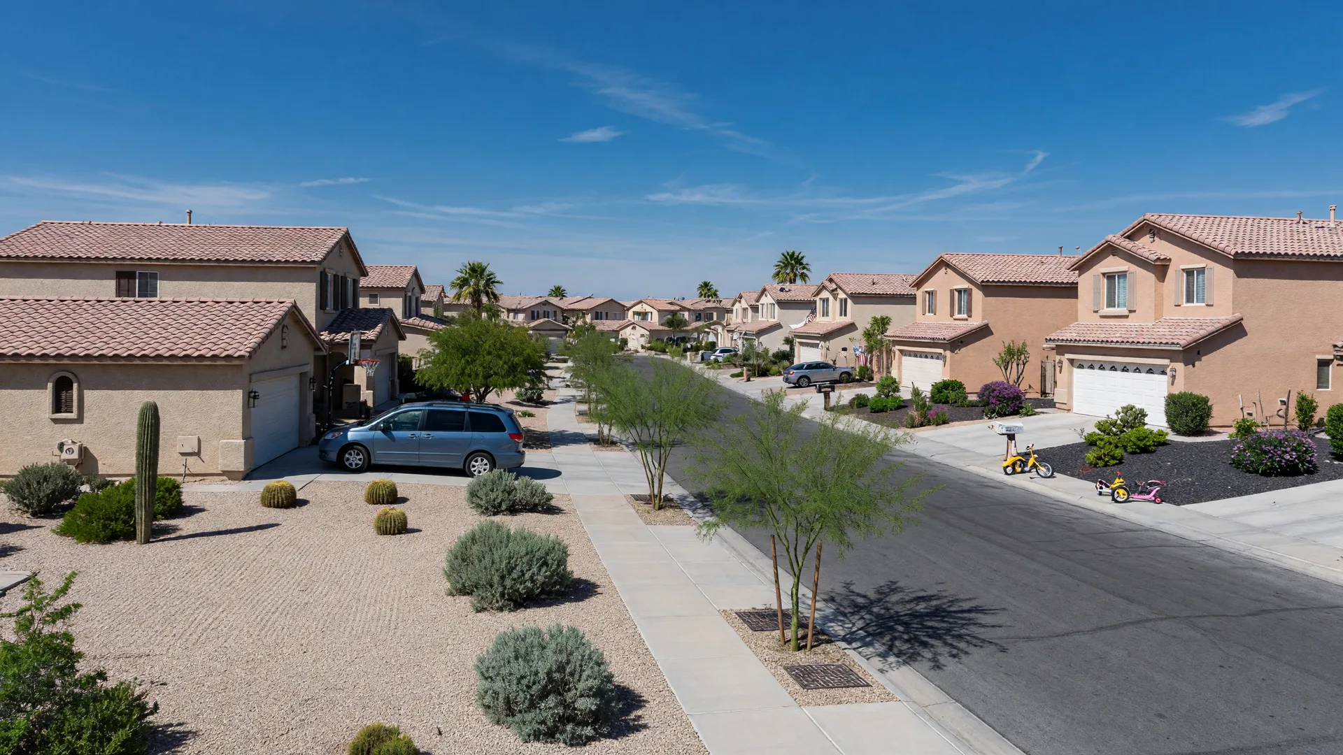 Mix of one- and two-story stucco homes with clay tile roofs and attached garages along a tidy desert-landscaped street in a 2000s Summerlin neighborhood