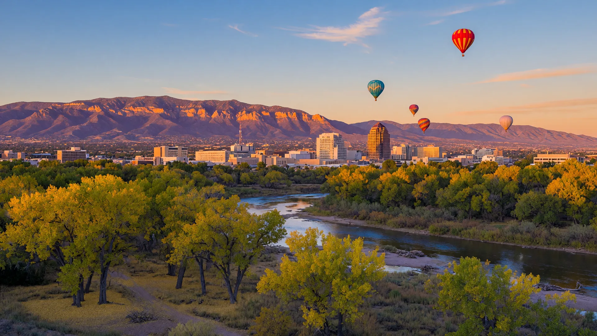 Hot air balloons rising over the Rio Grande bosque at golden hour with the Sandia Mountains glowing in the background