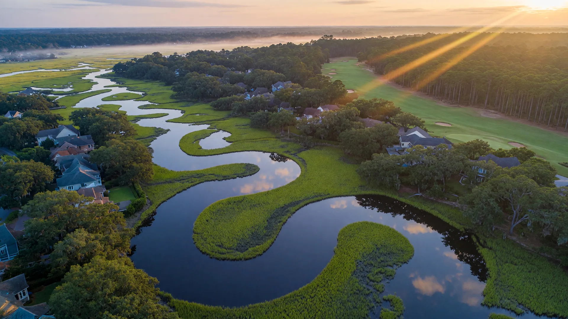 Aerial view of a Lowcountry coastal community at dawn, homes tucked among live oaks and marsh-lined waterways