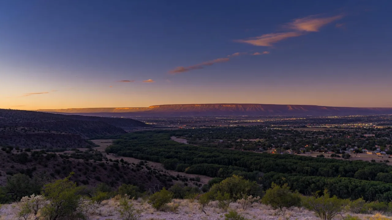 Dusk over the Rio Grande valley, with the cottonwood bosque and the first city lights of Albuquerque