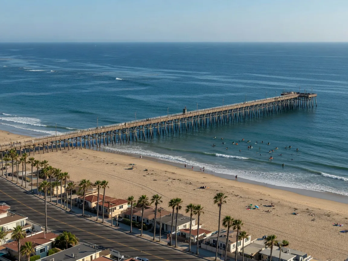 The Imperial Beach Pier over the Pacific on a late-September afternoon, with surfers past the pilings and the palm-lined, sandy Seacoast Drive curving along the shore in ZIP 91932