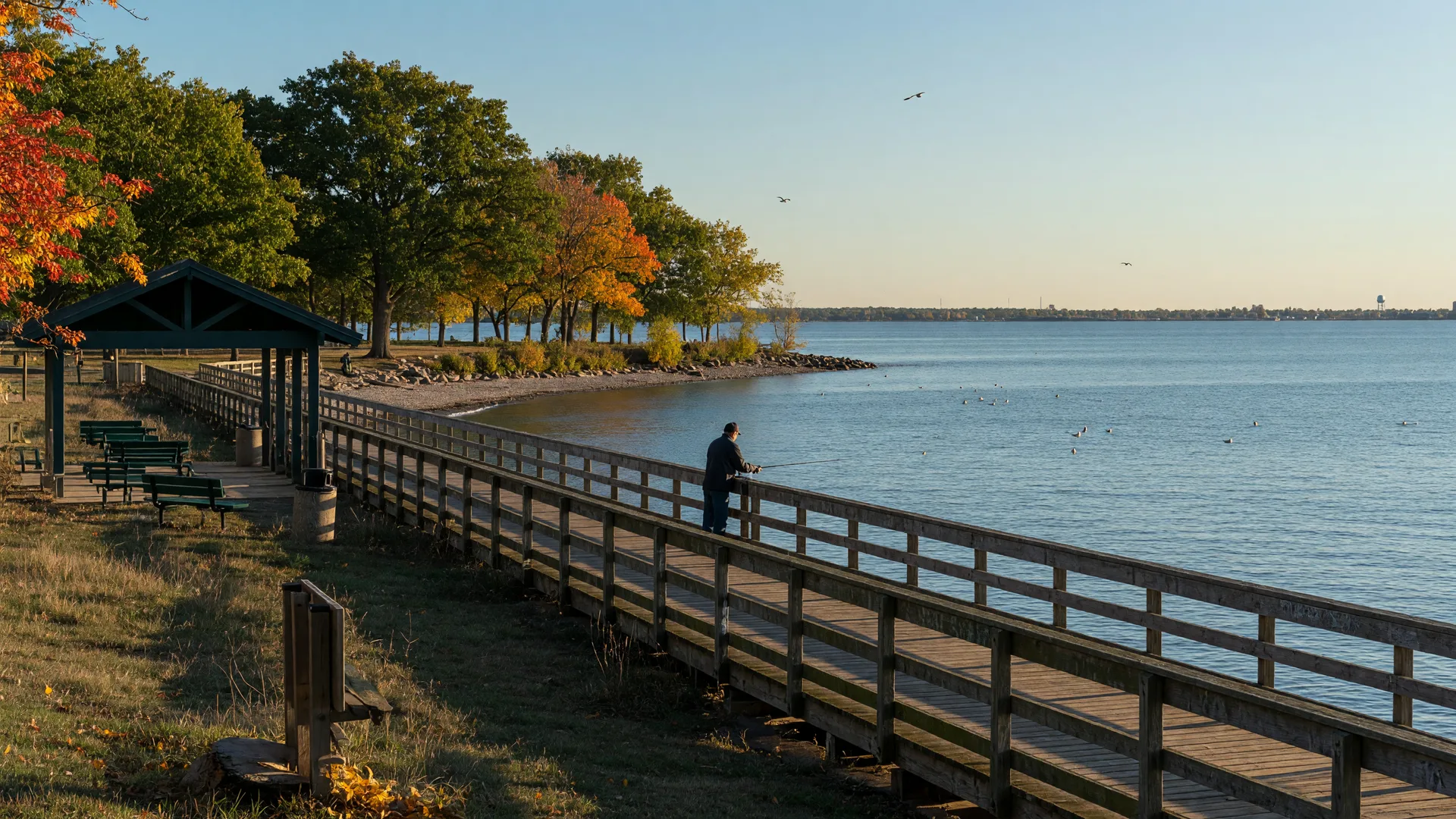 A wooden fishing pier extending over Lake Erie beside autumn trees in Euclid's Sims Park at golden hour