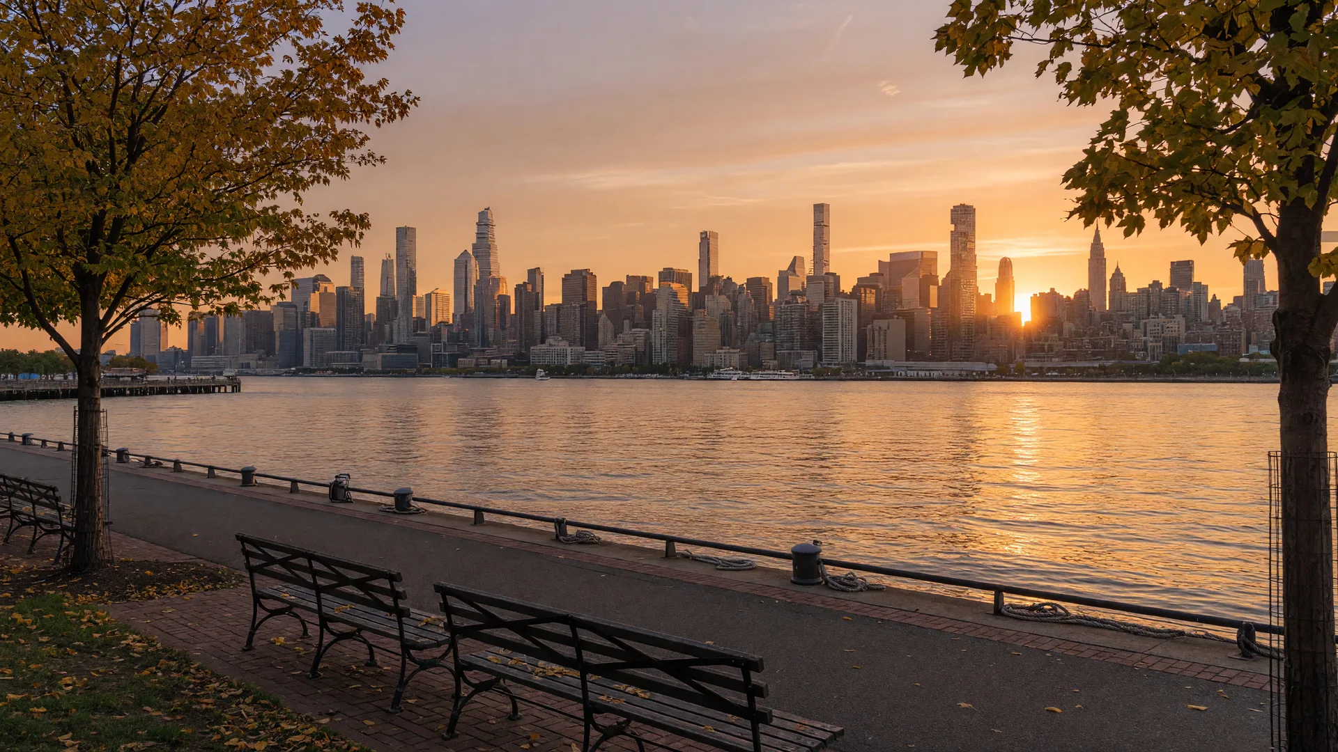 New York City skyline viewed from the Hudson River waterfront at golden hour with warm light reflecting on the water
