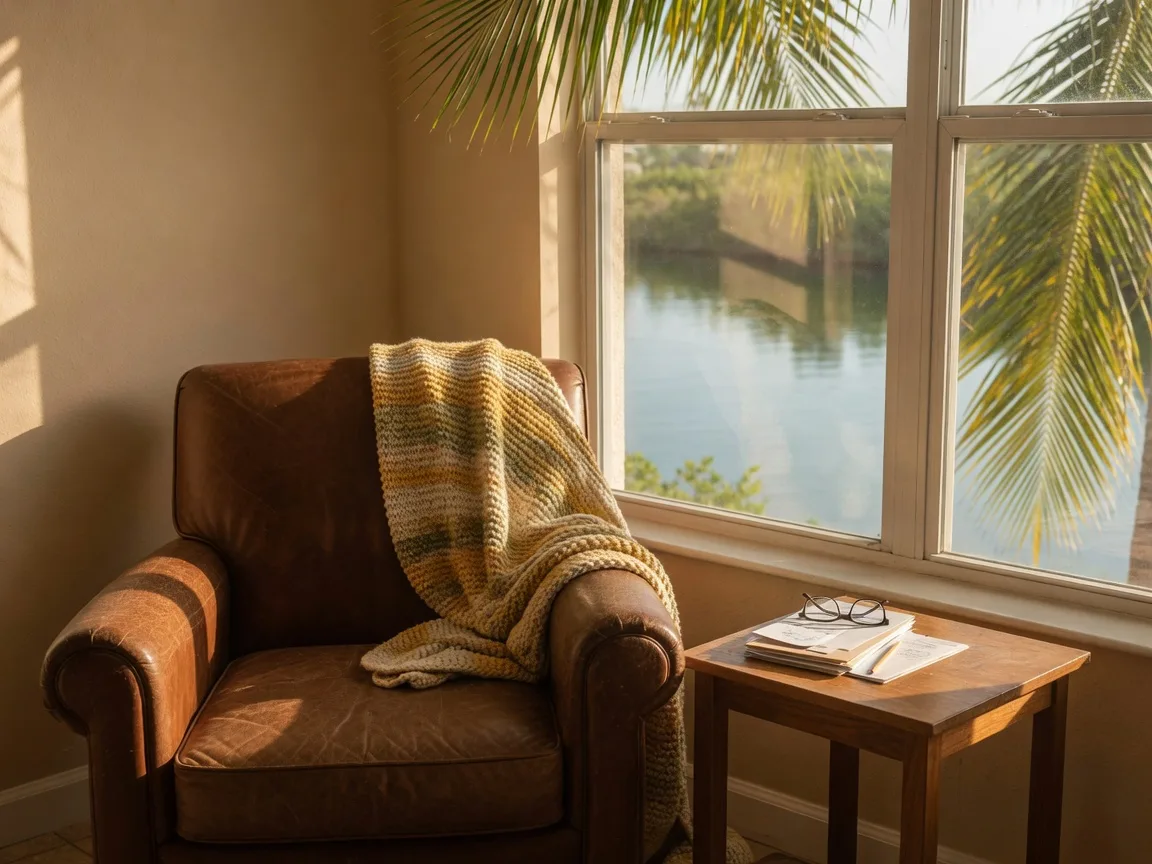 A reading armchair beside a window overlooking a calm Florida intracoastal canal, reading glasses on a side table.