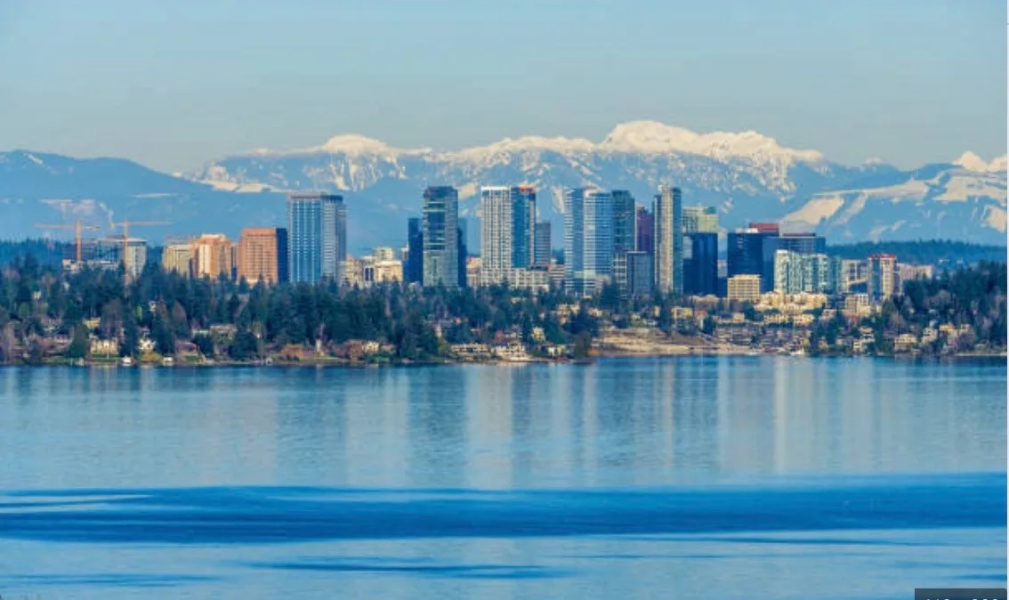 Panoramic view of the Bellevue skyline with snow-capped mountains reflected in calm water