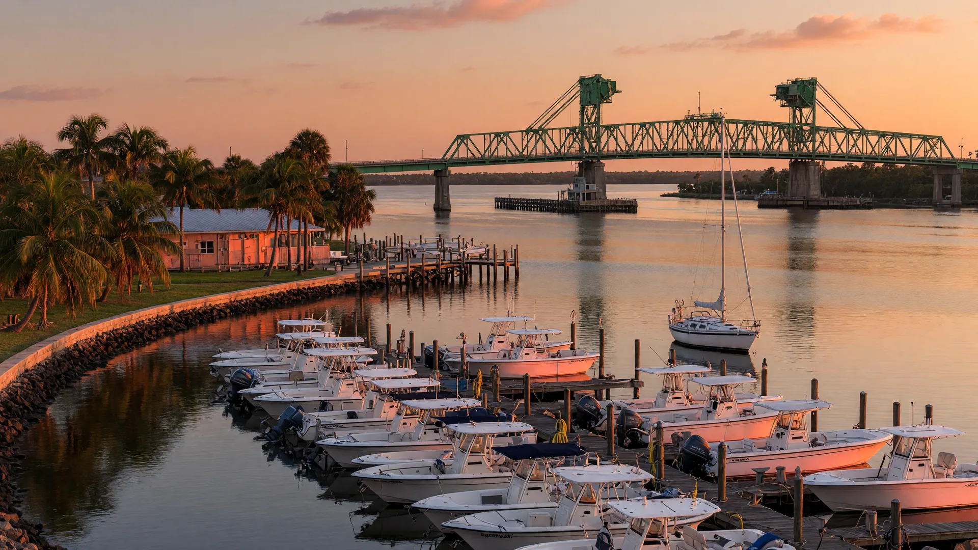 Boats moored at a marina on the Manatee River in Bradenton at golden hour, with the Green Bridge crossing the river in the distance