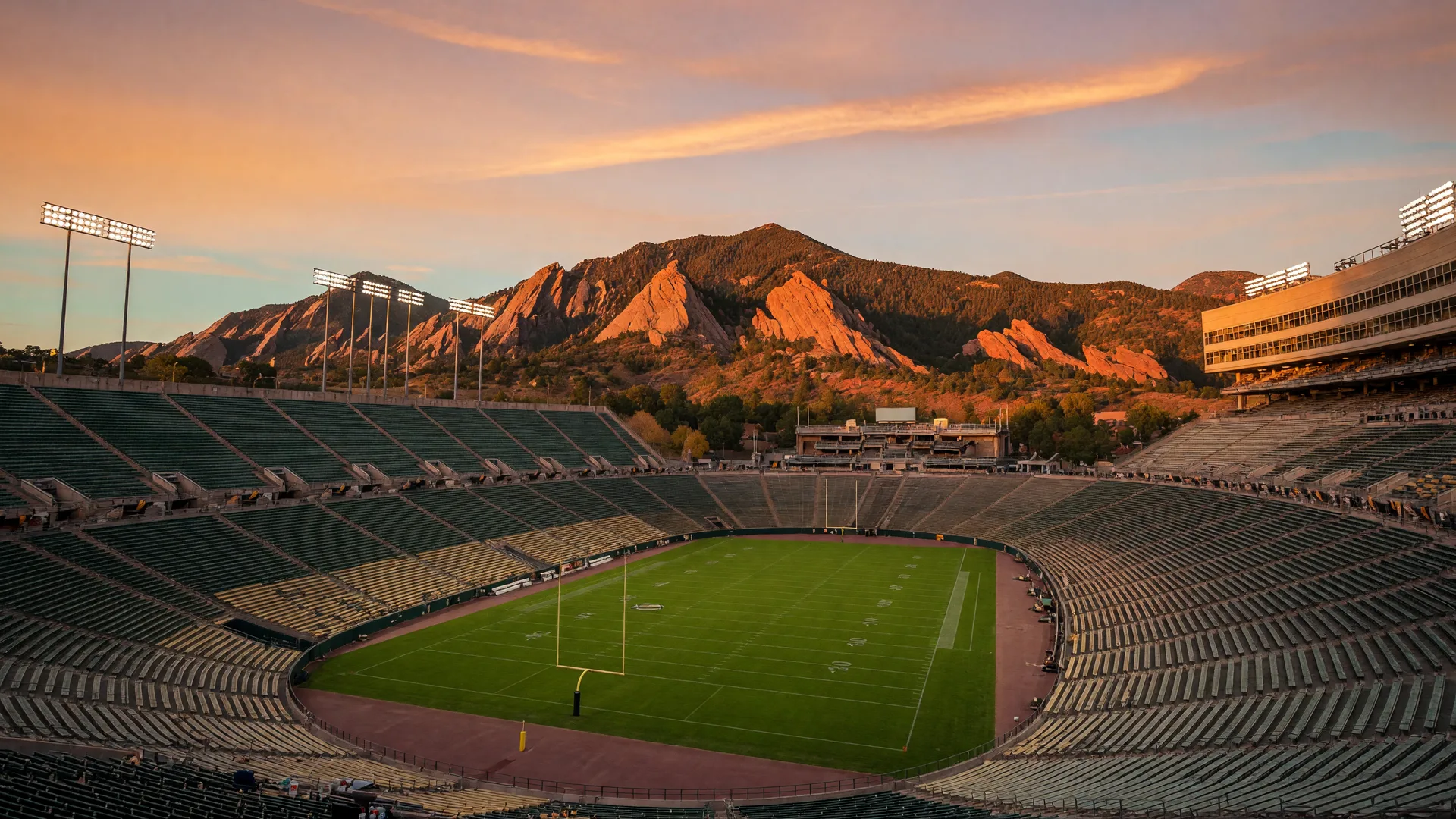 A college football stadium bowl at golden hour with the flatiron mountain ridge of the Colorado Front Range rising behind it