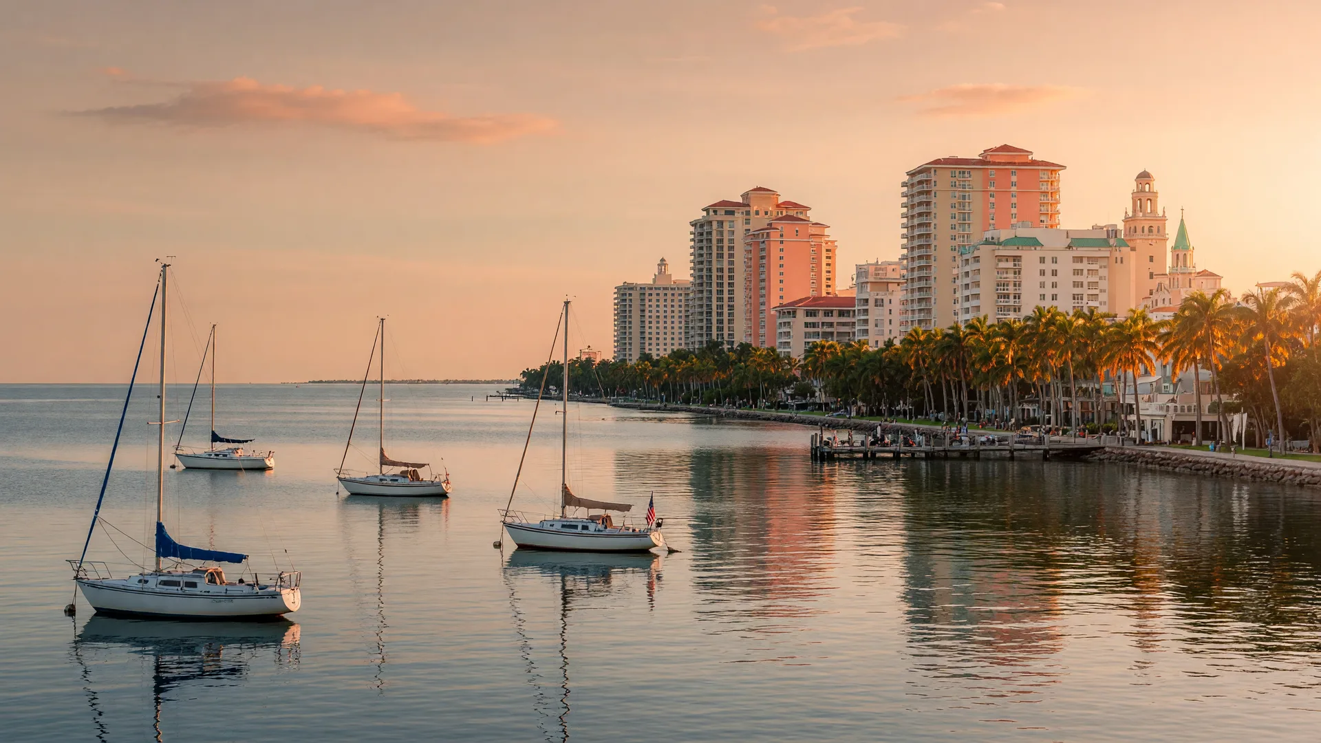 The Naples, Florida waterfront skyline at golden hour across the bay, with sailboats moored in the foreground and warm light on the water