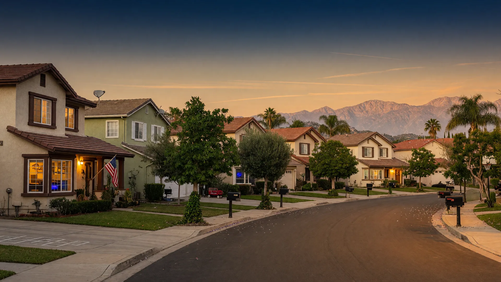 A quiet Southern California neighborhood at golden hour, homes with warm lights, trees, and mountains in the distance