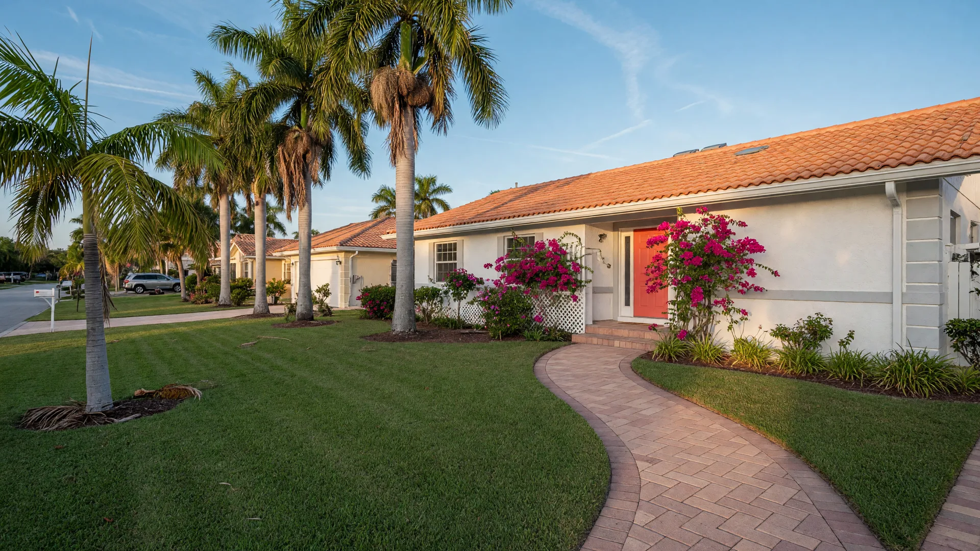 Welcoming single-family Florida home in a quiet Naples neighborhood with a white facade, barrel-tile roof, palm trees, and a clear blue sky at late afternoon