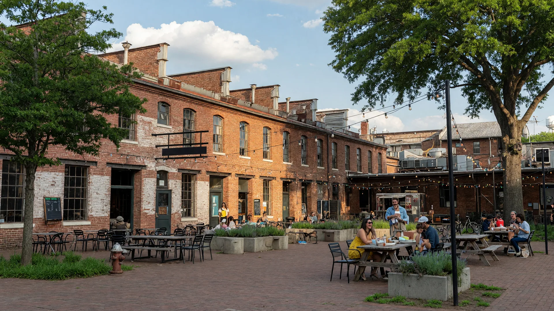 Optimist Hall food hall in Optimist Park Charlotte NC with red brick textile mill architecture and outdoor seating under string lights