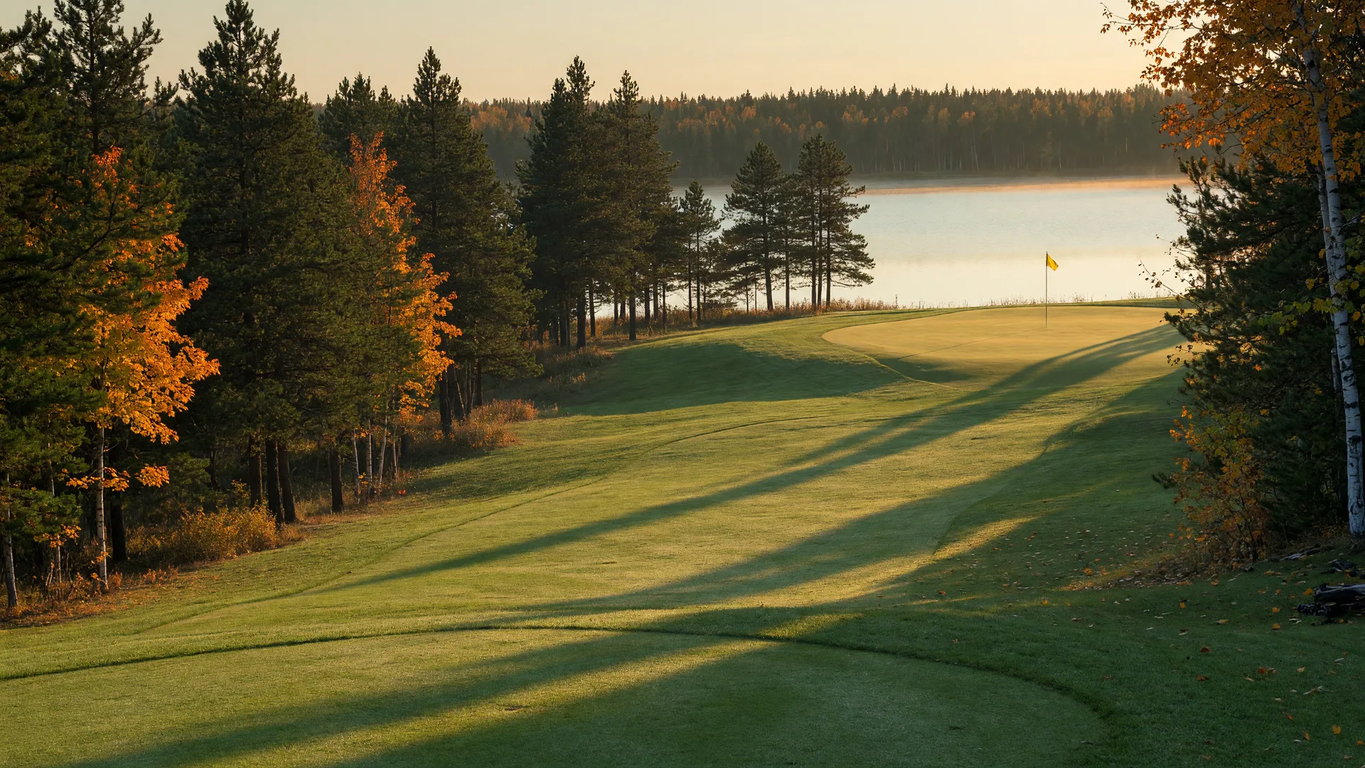 A fairway on a northern Minnesota golf course in late September with turning orange and gold maples and a lake with pine shoreline in the distance