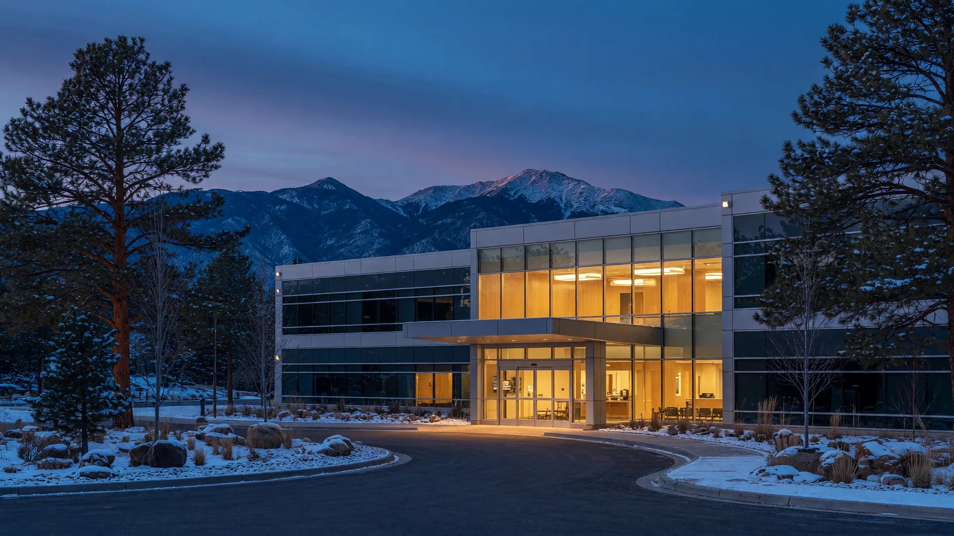 A modern regional hospital campus glowing at blue hour with ponderosa pines and the San Francisco Peaks on the horizon near Flagstaff