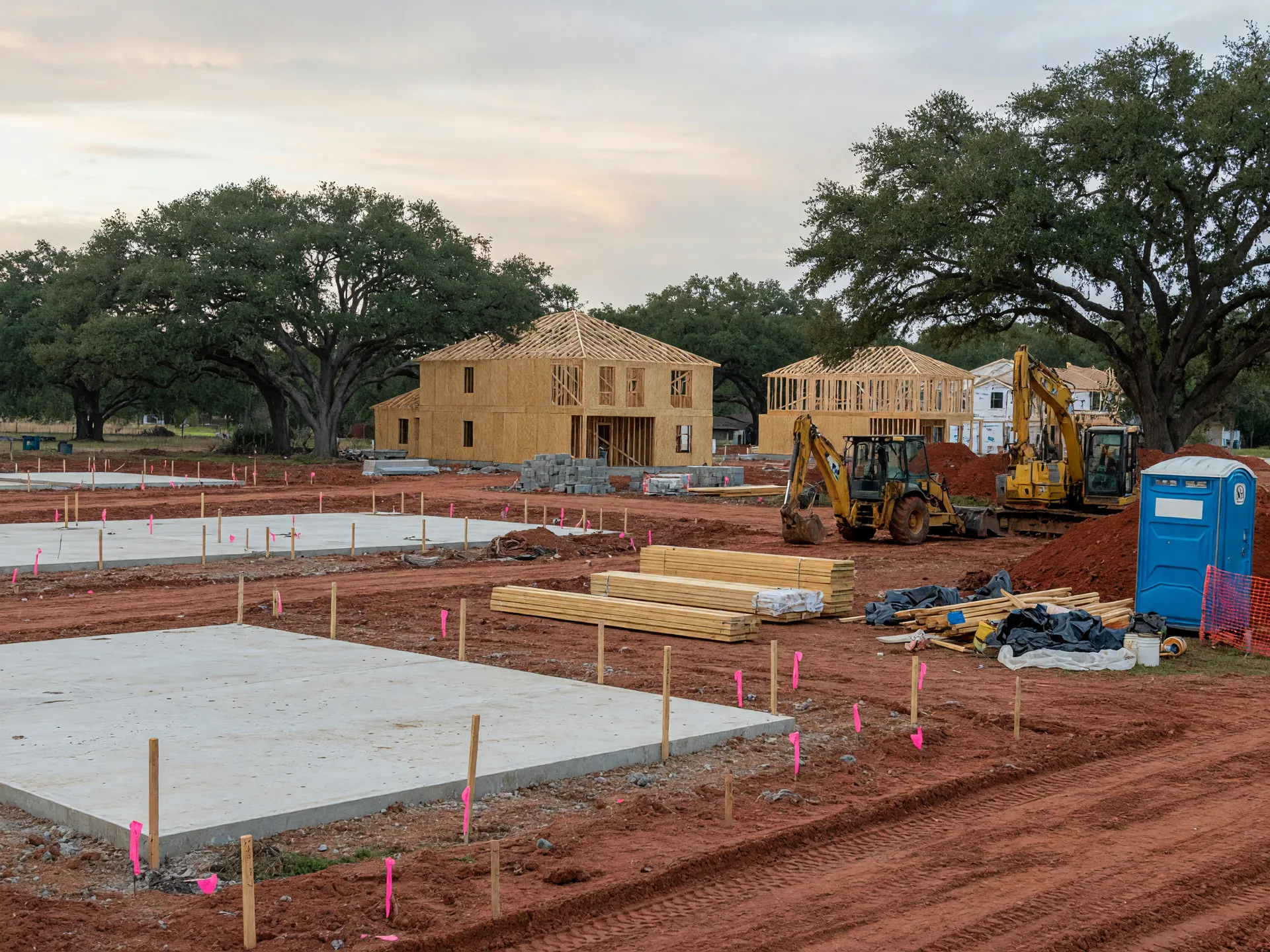 Residential construction site in a developing Texas subdivision with concrete foundations and wood-framed houses under construction