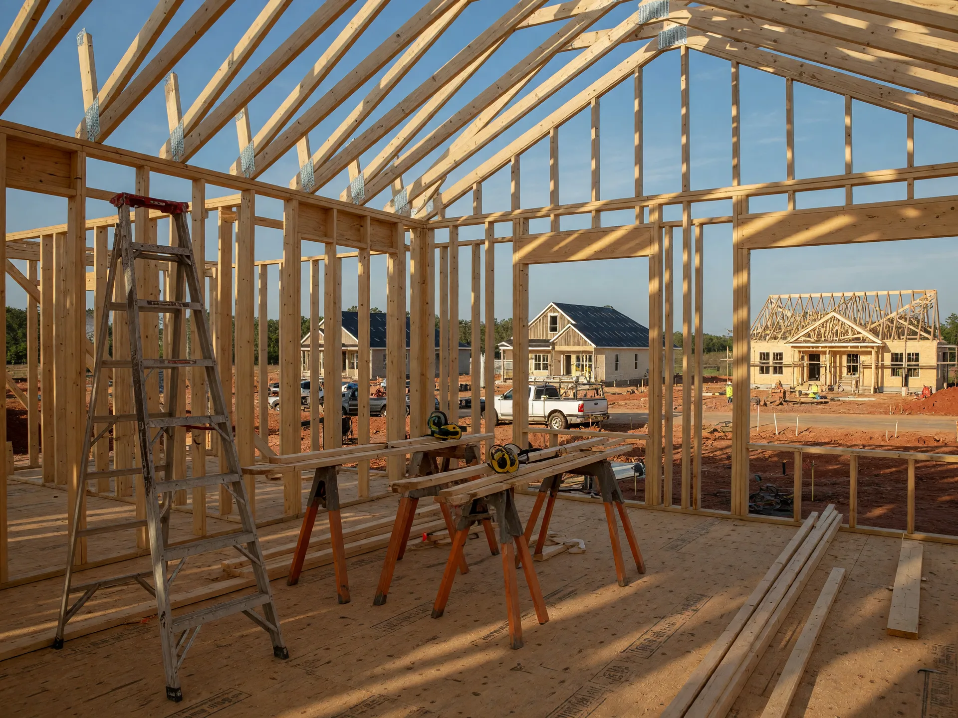 A new home under construction in the framing stage, timber studs and roof trusses open to a clear blue sky