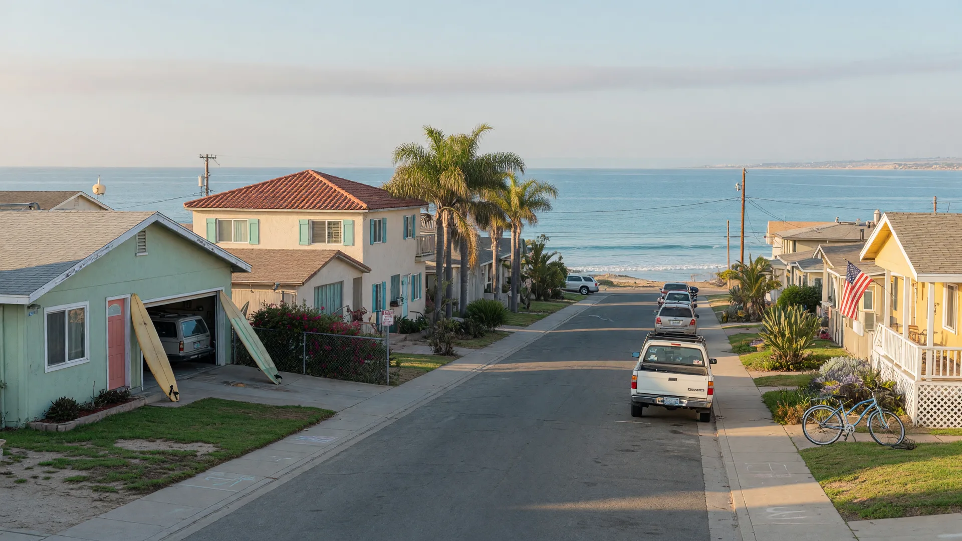 A quiet coastal residential street in Imperial Beach, California on a September morning, with low beach homes, palm trees, and ocean light at the end of the block in ZIP 91932
