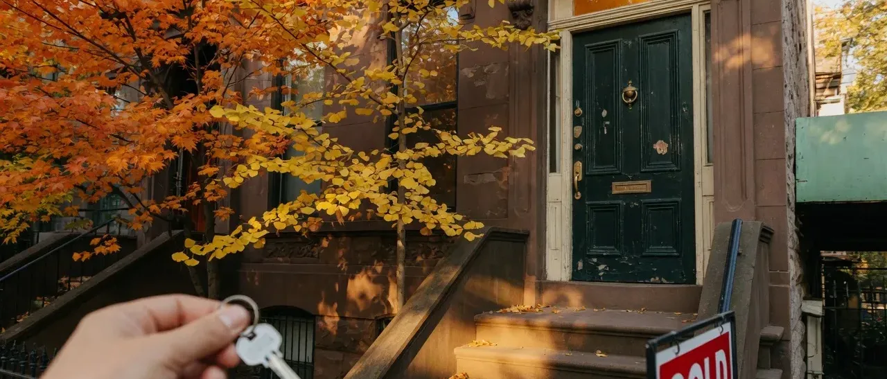 Classic home entrance on an autumn afternoon with key in hand and a sold sign in the foreground