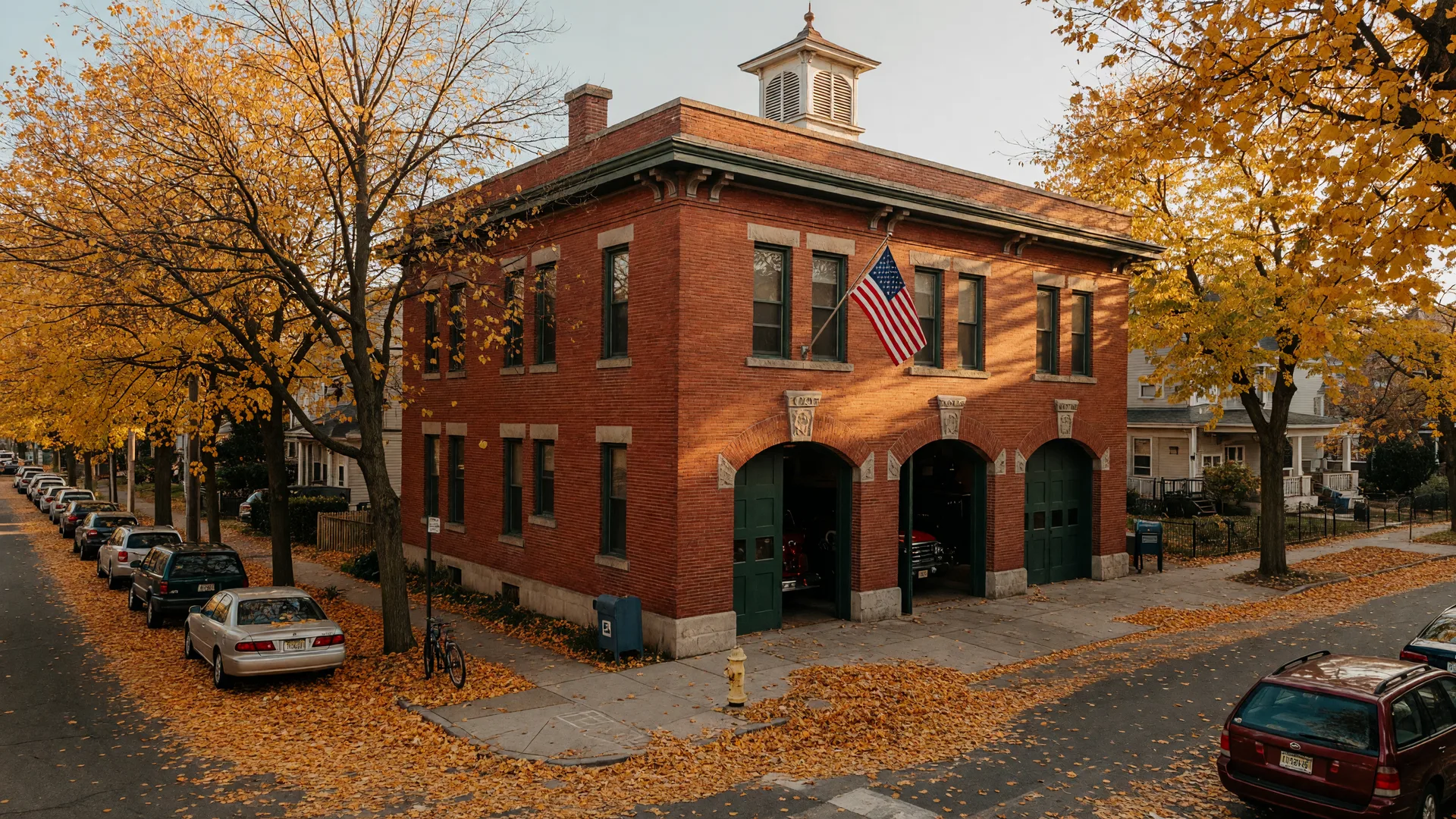 The historic 1901 red-brick Fire Station 3 on Harrison Avenue in the Montclair Fourth Ward with arched bay doors, stone lintels, a small cupola, and an American flag in warm October light
