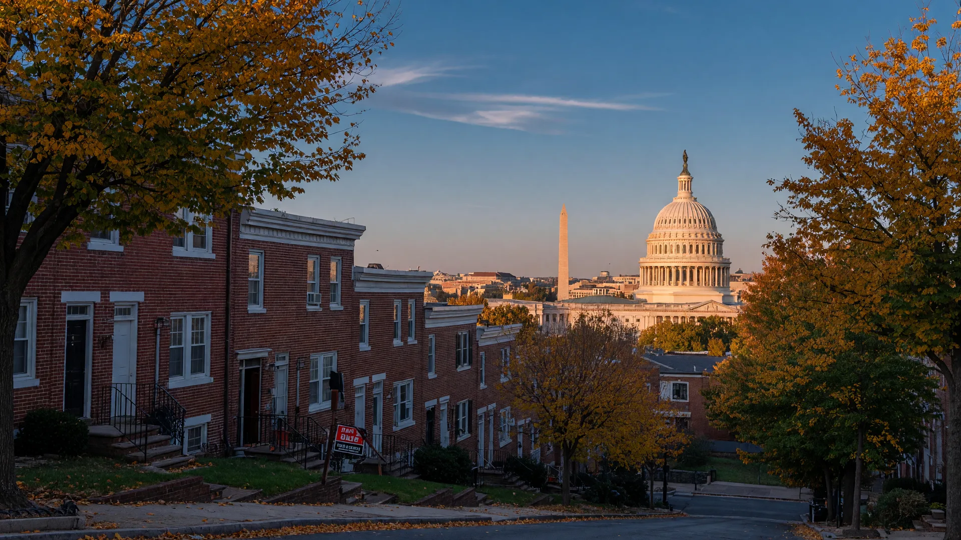 The Washington, DC skyline in early autumn seen from a leafy residential street with brick rowhouses and a for-sale sign in the foreground