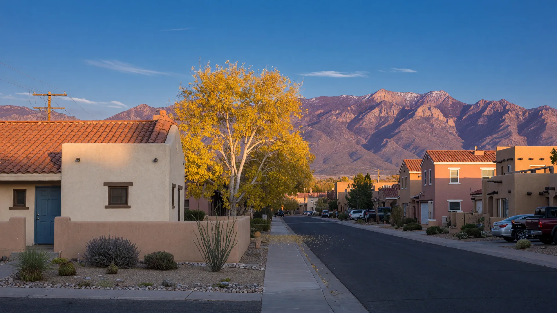 A quiet Albuquerque residential street on a crisp October morning, southwestern stucco homes with terracotta roofs, golden cottonwoods, and the Sandia Mountains under a clear blue sky