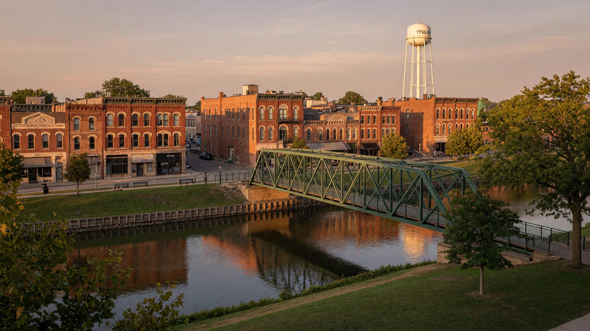 Historic brick buildings along the Huron River in Depot Town, Ypsilanti with a pedestrian bridge and the water tower in the distance