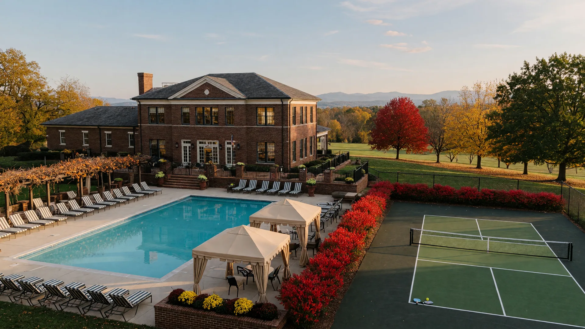 A resort-style clubhouse pool and pickleball court at an active adult community with autumn trees in the background