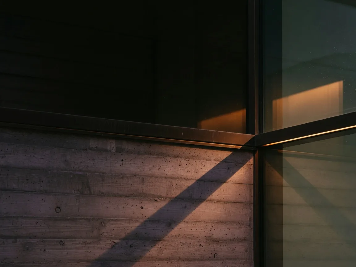 Architectural detail of board-formed concrete meeting dark bronze trim at dusk