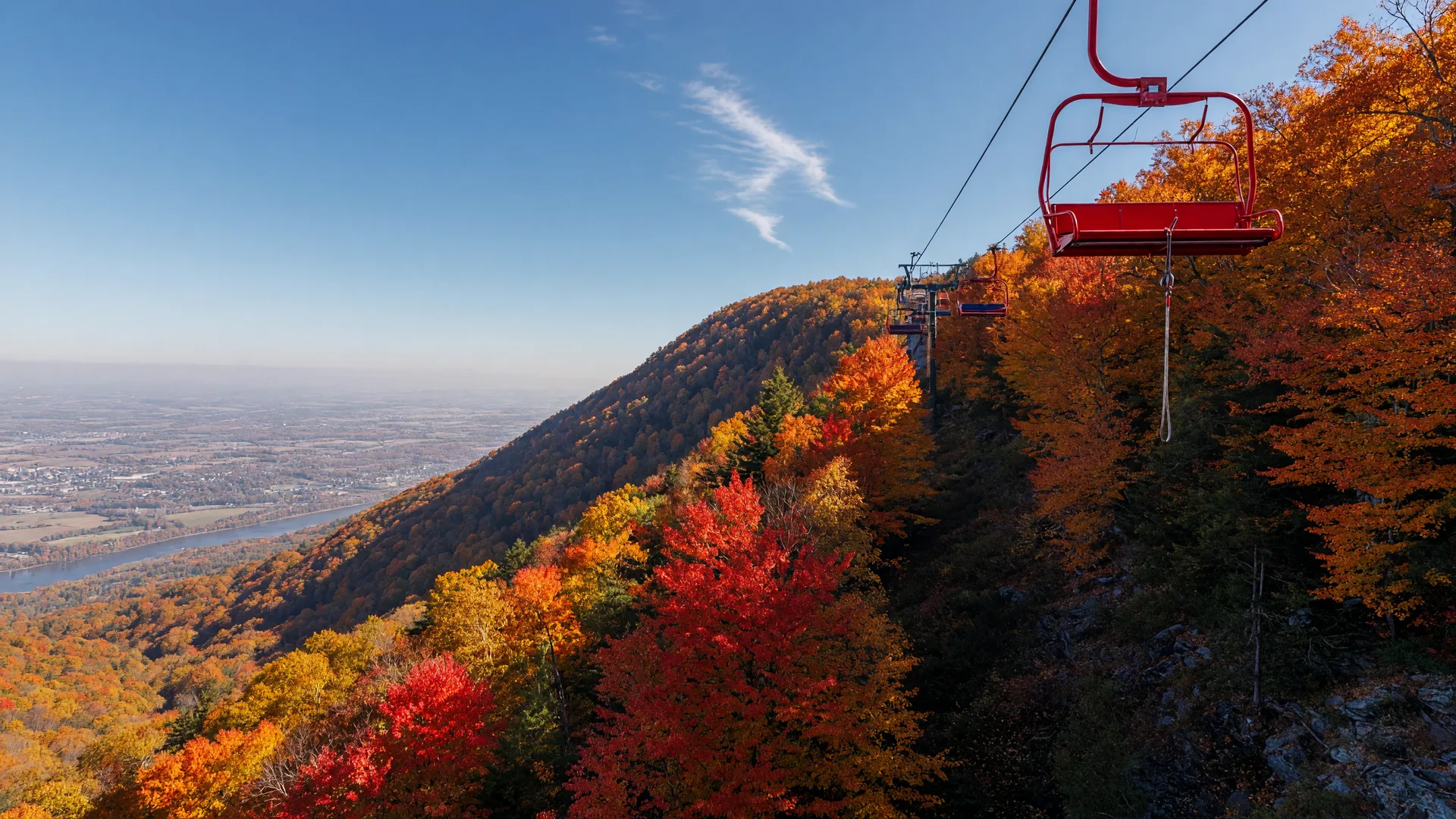 A red chairlift cabin climbing above the Blue Mountain ridge in peak October color, with the hazy Lehigh Valley visible far below