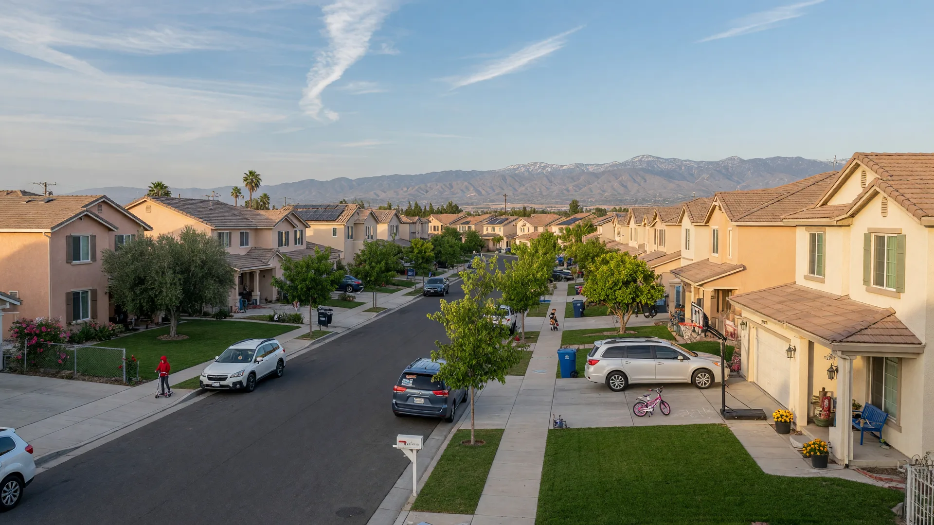 A tree-lined, family-friendly residential street in Northwest Fresno 93722 with newer stucco homes and late-afternoon light