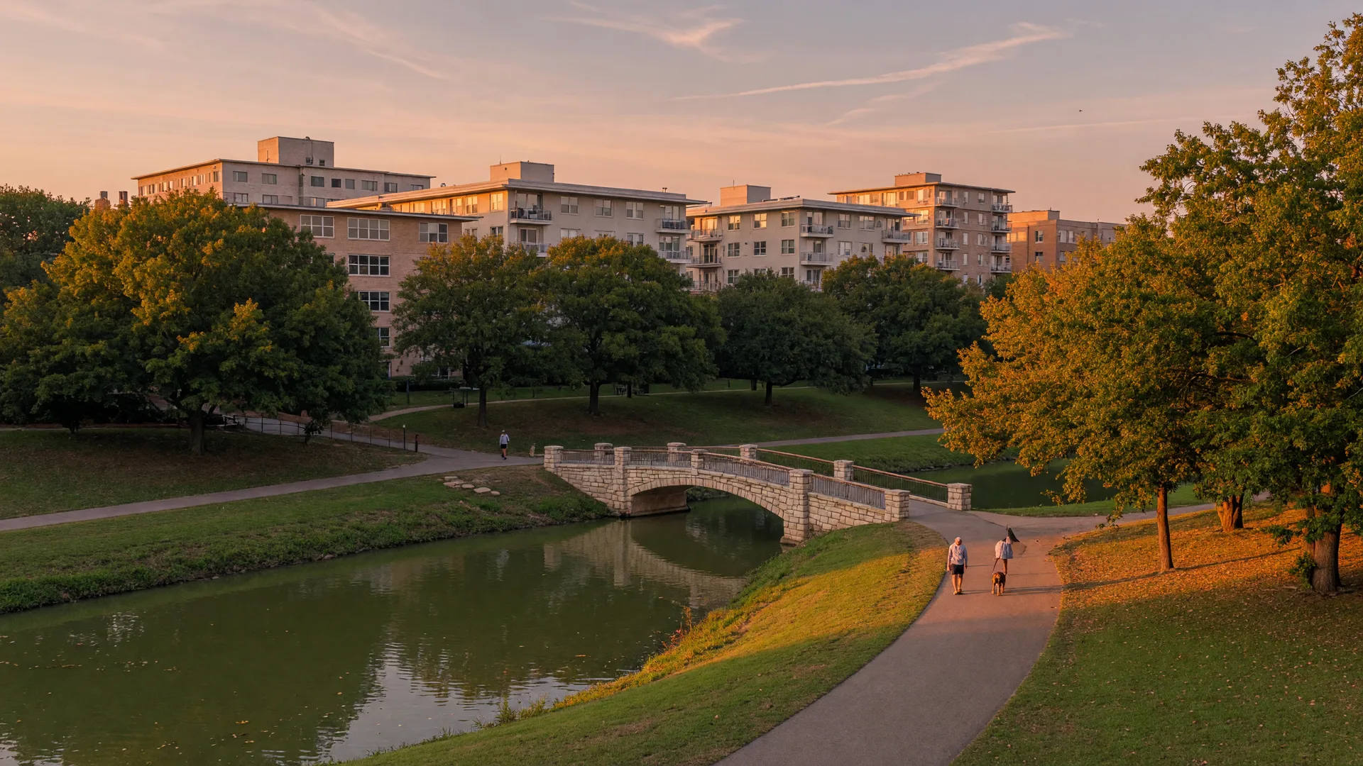 A tree-lined walking path along Turtle Creek in Oak Lawn Dallas with mid-century condos rising behind the trees at dusk