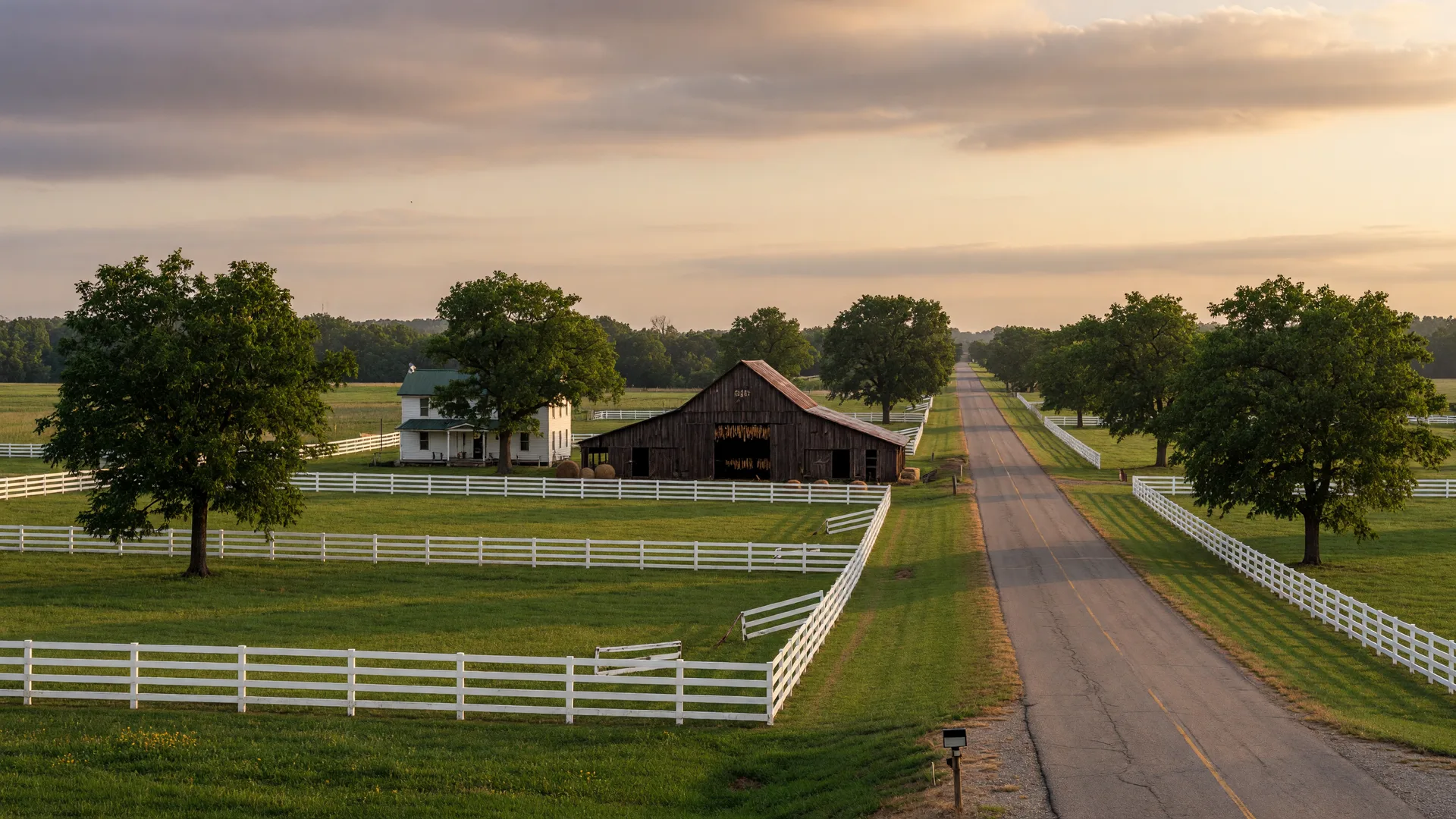 A long country road lined with white plank fences near Rockfield with farmland and a farmhouse in golden light