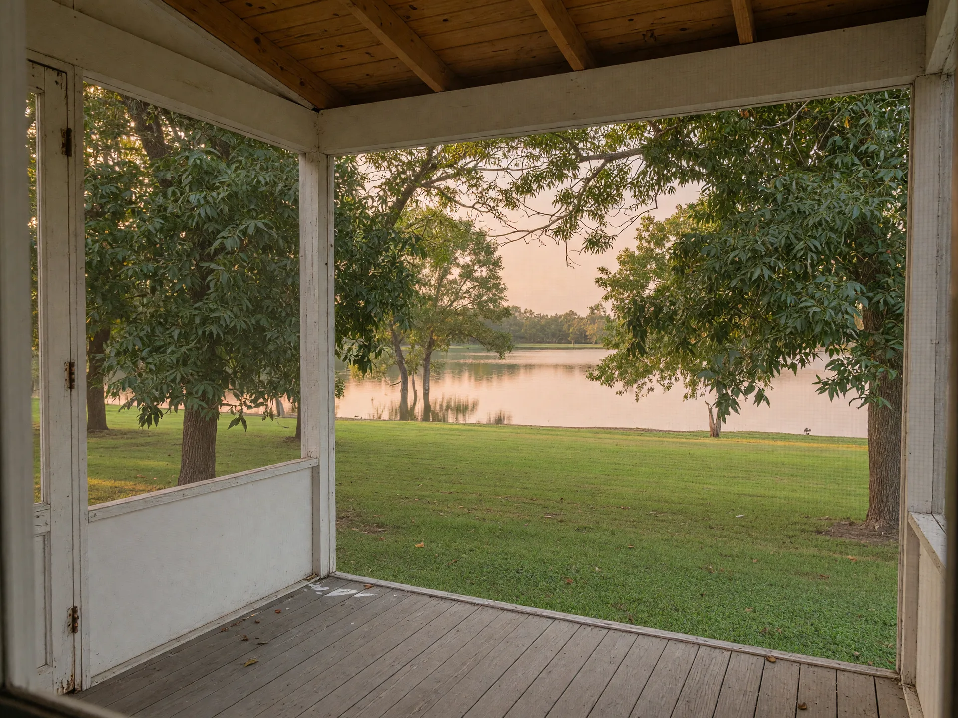 View through a screened porch screen toward pecan trees and the lake