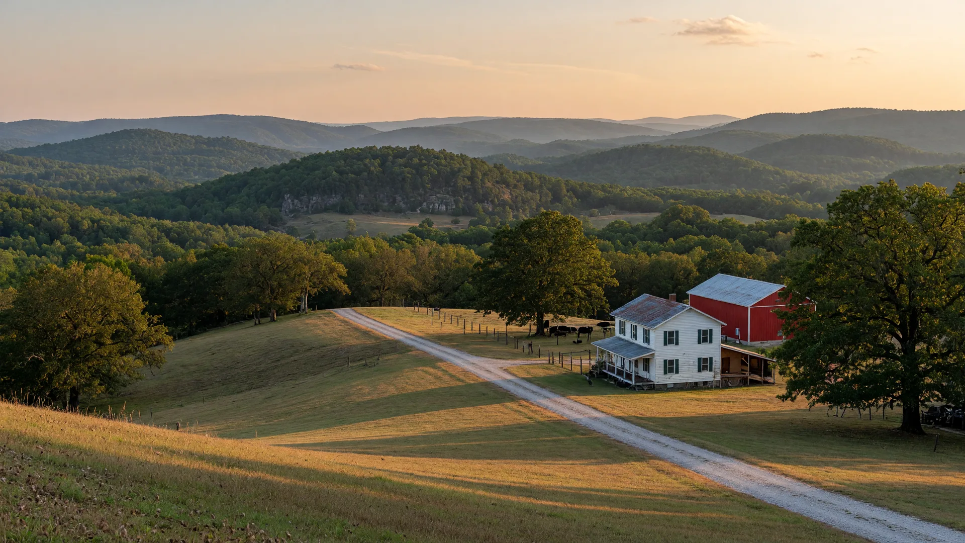Rolling green Ozarks hills at golden hour with a gravel driveway leading to a white farmhouse and red barn