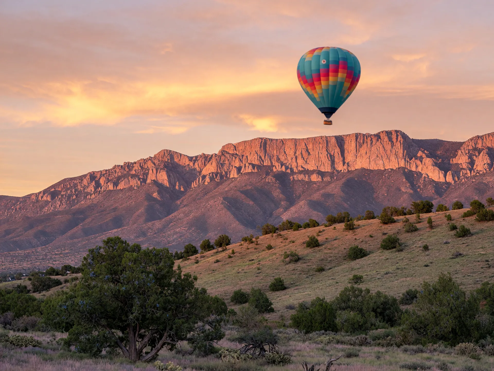 A hot air balloon floating above the Sandia Mountains at sunrise near Albuquerque, New Mexico