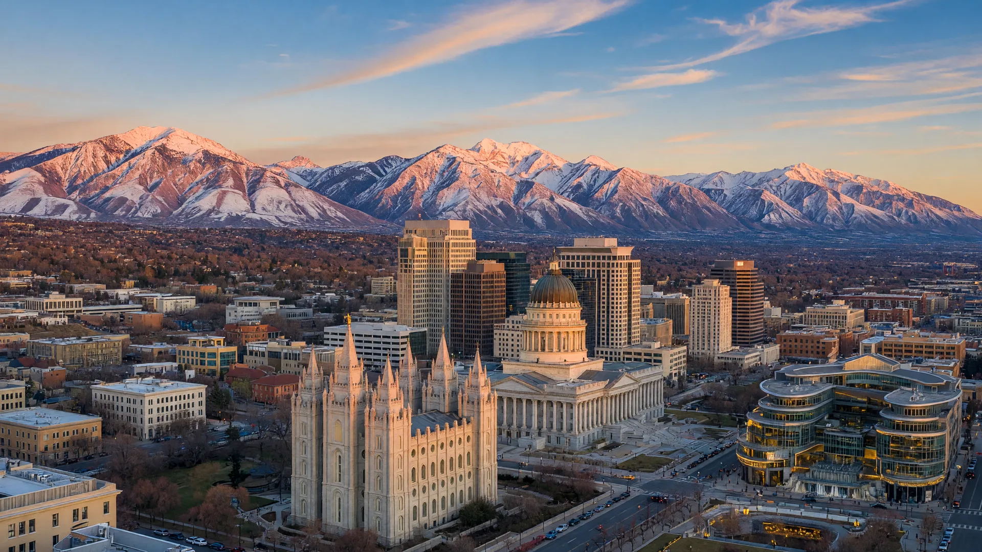 Salt Lake City skyline with the Salt Lake Temple and State Capitol against the towering Wasatch Mountains at golden hour